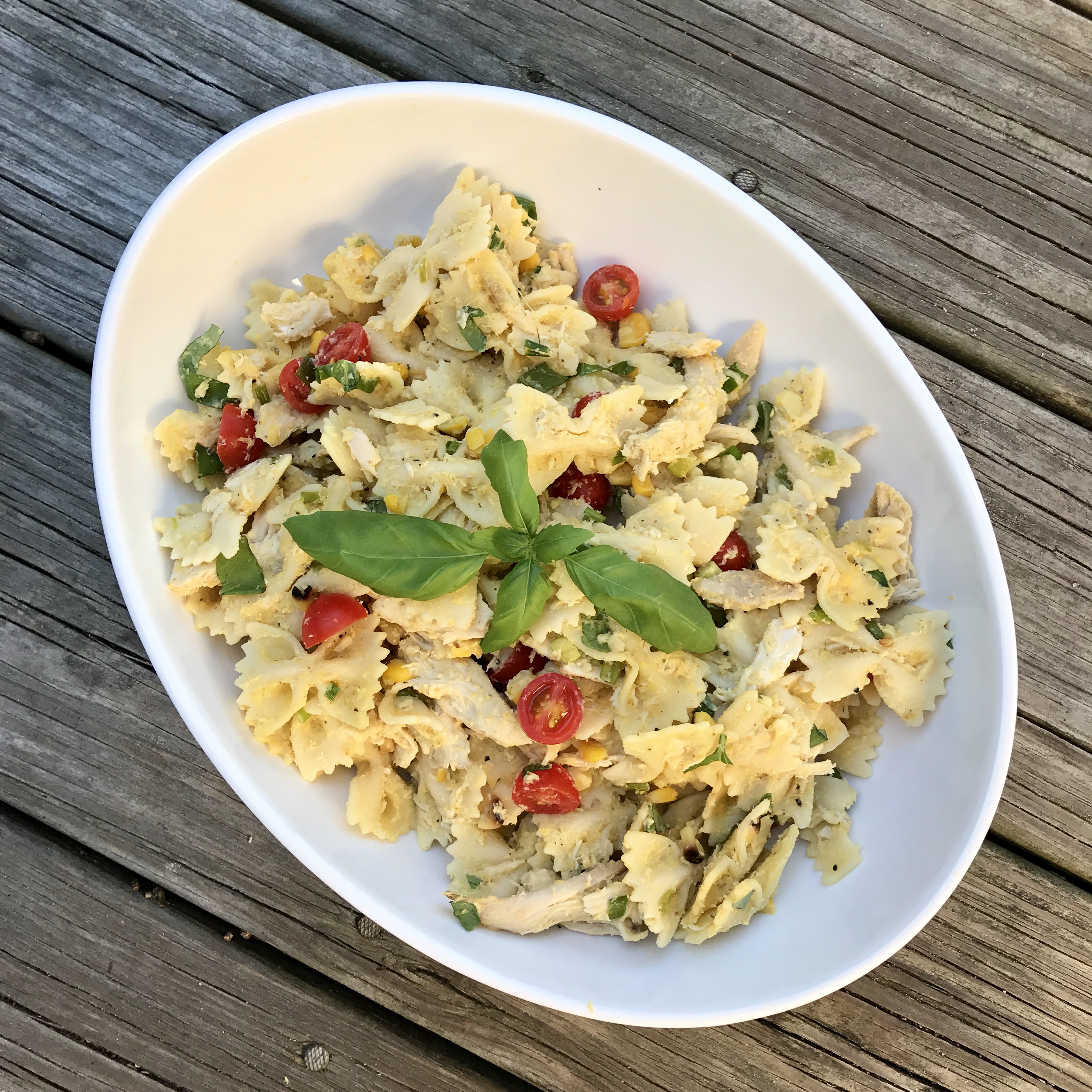 White bowl filled with Summer Corn Pasta with Basil, garnished with fresh basil leaves on top.