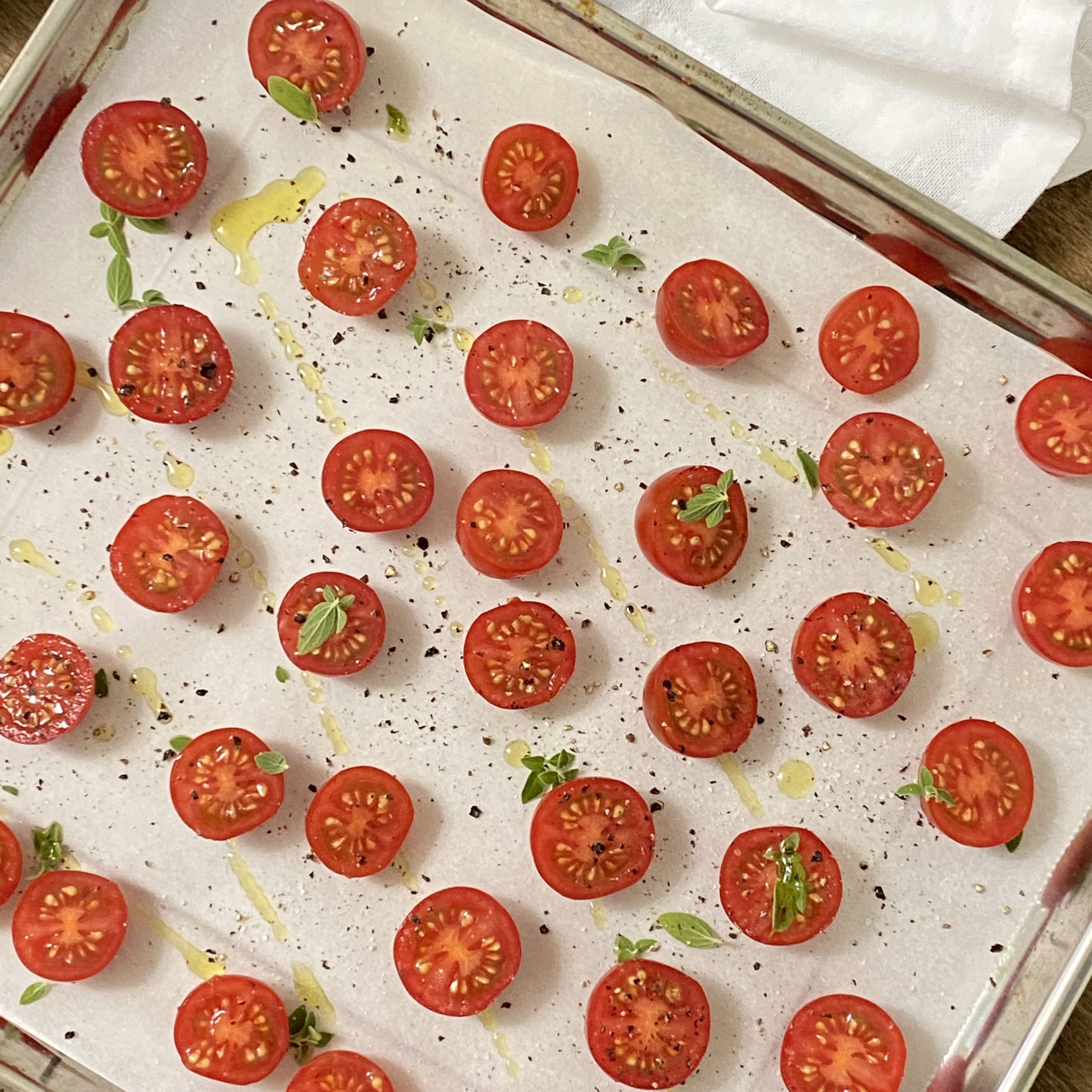 Cherry tomatoes on a baking sheet lined with parchment drizzled with olive oil, salt, pepper, and oregano leaves.