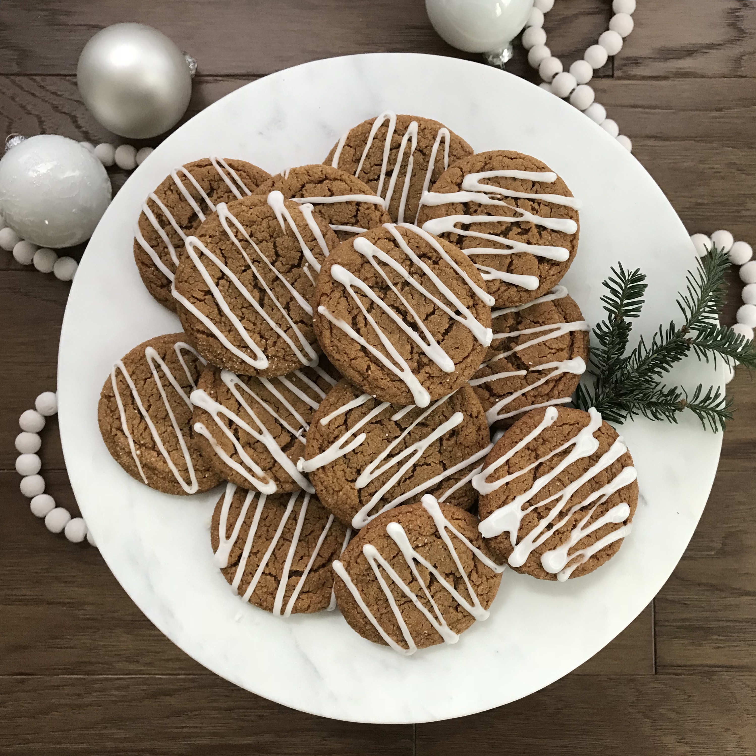 Iced ginger cookies on a white plate next to white ornaments and pine bows.