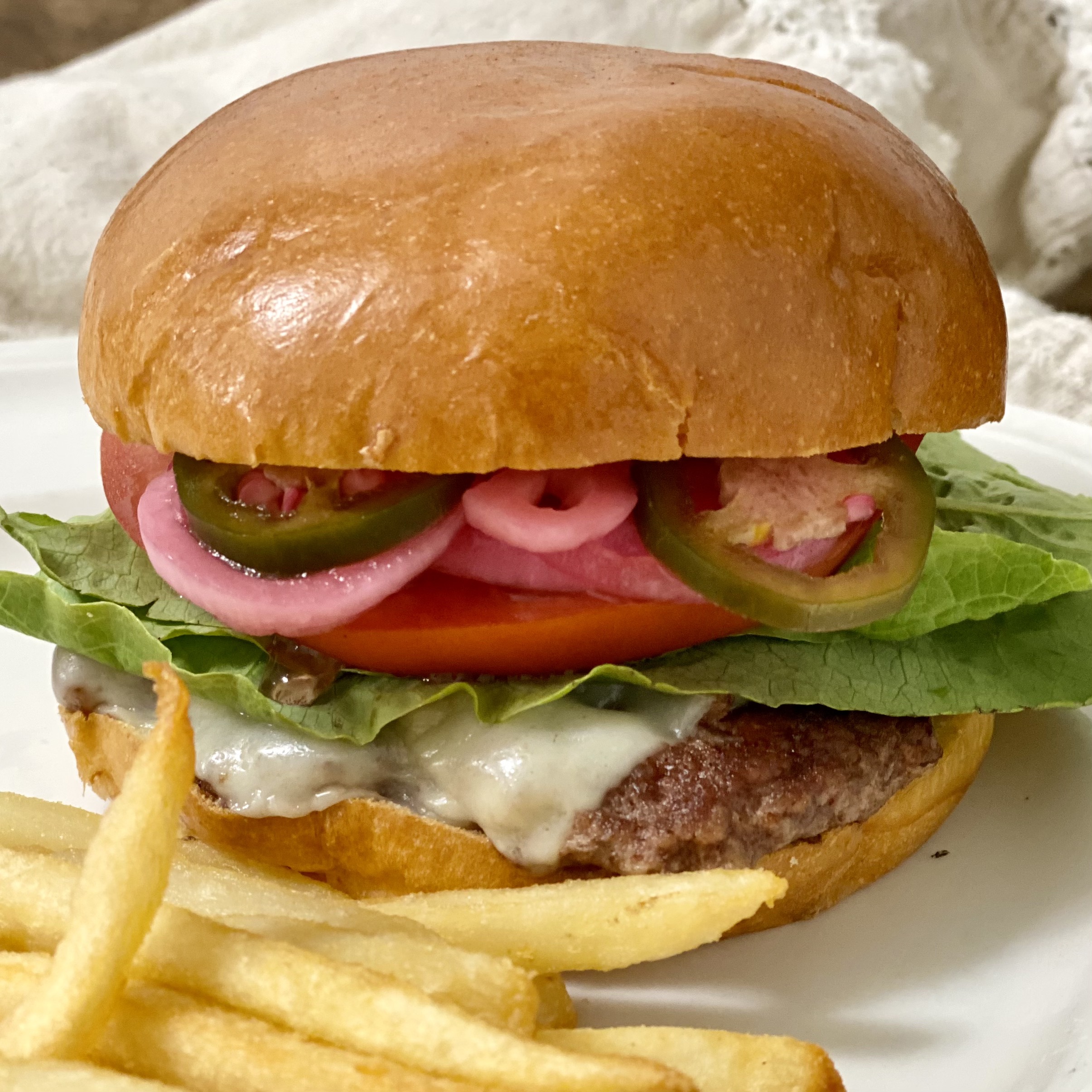 A cheeseburger with pickled red onions, lettuce and tomato on it.