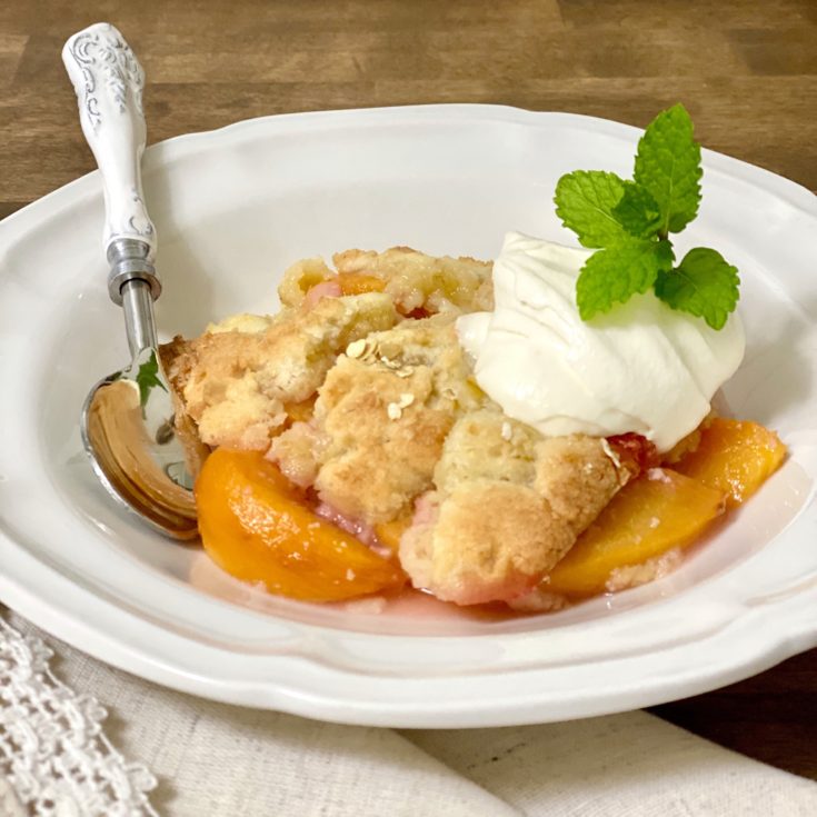 Peach cobbler with Bourbon Cream in a white bowl with a mint spring on top.