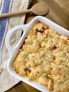 Peach cobbler with bourbon cream in a white baking dish ready to be served.