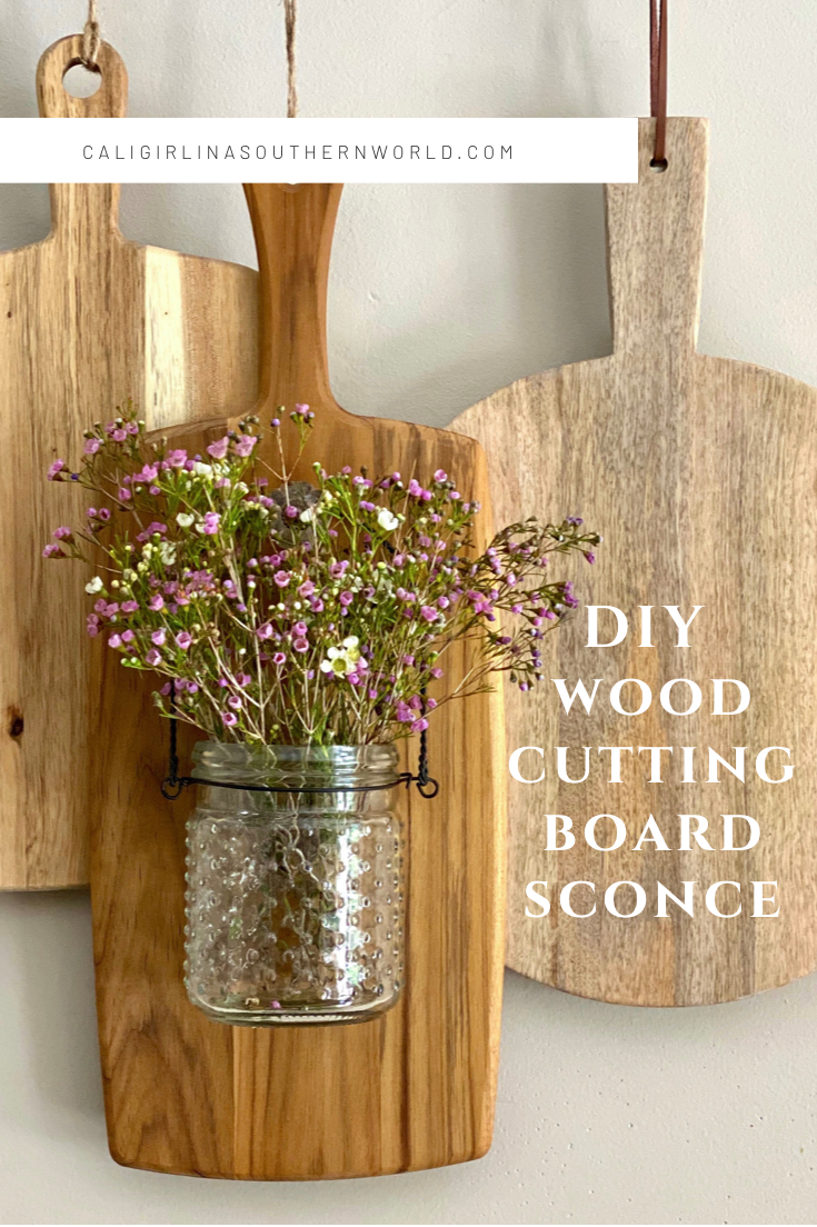 Wood cutting boards hanging on the wall. One is a sconce with flowers in it.