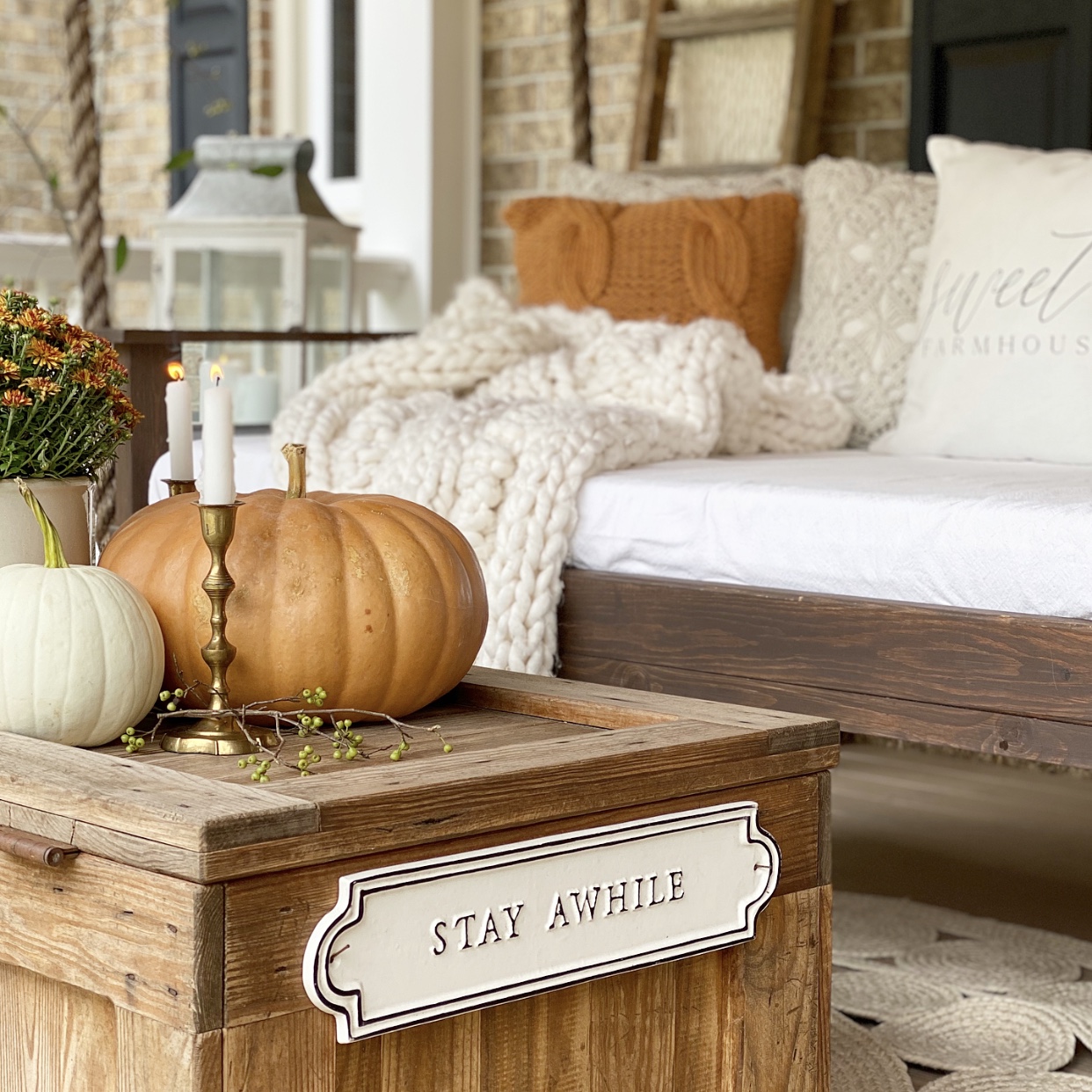 Front porch swing bed with cozy Fall pillows and a blanket. Candles and pumpkins sit atop the coffee table.