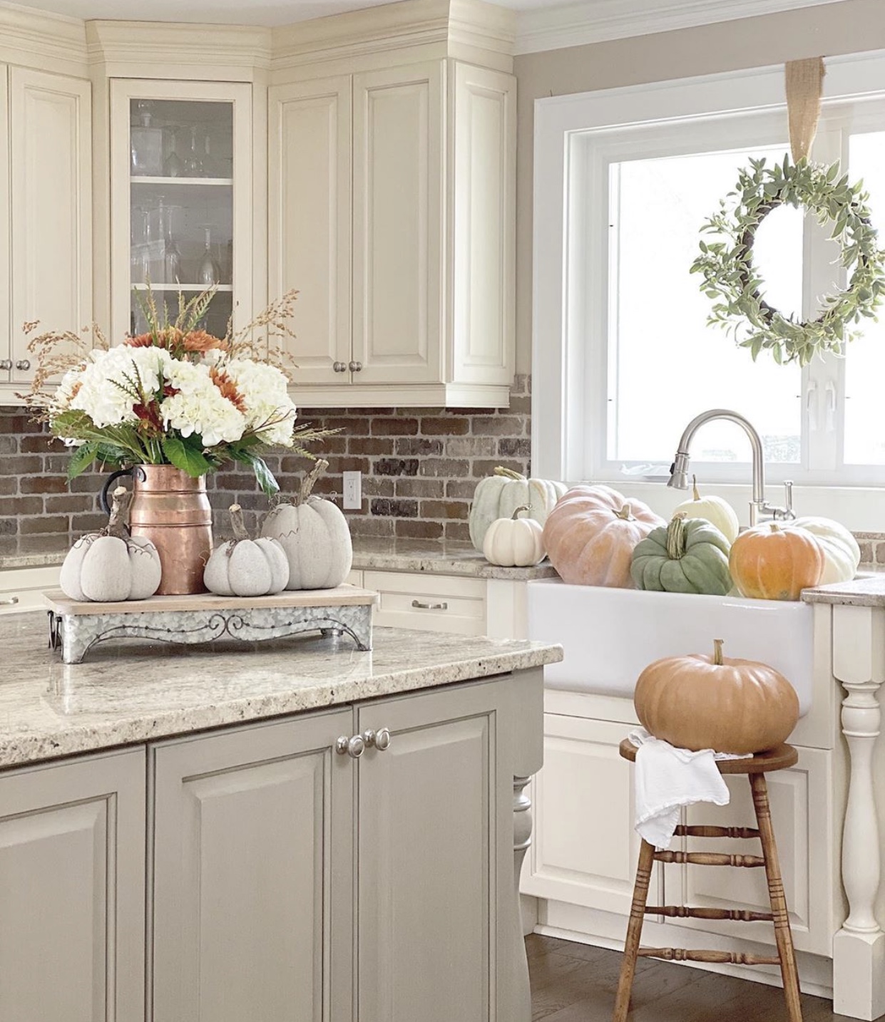 Kitchen with pumpkins in the farmhouse sink and a Fall floral arrangement on the island with concrete pumpkins.
