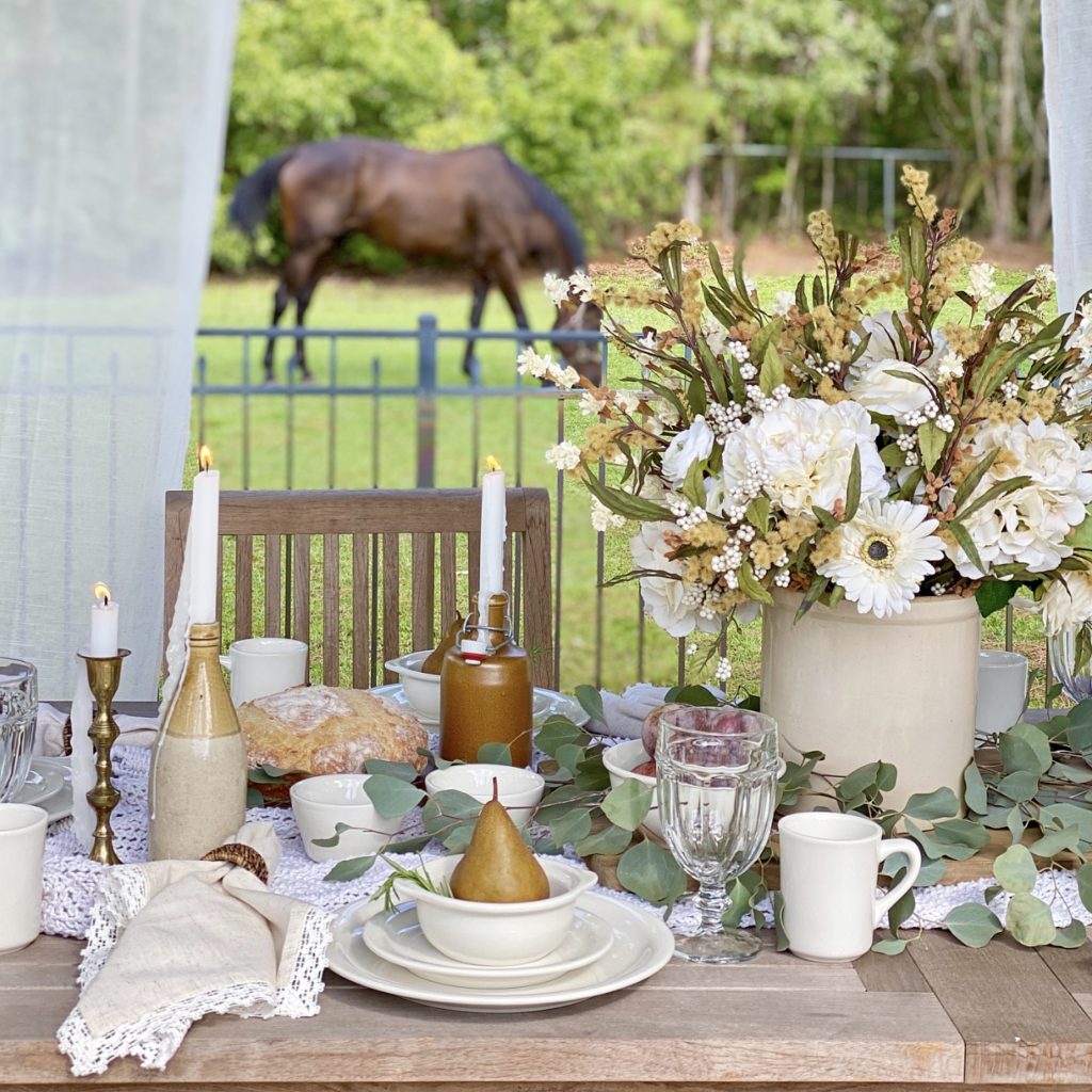 An early fall tablescape featuring neutral florals, eucalyptus, and pears on the table outside. A horse is in the grass in the background.