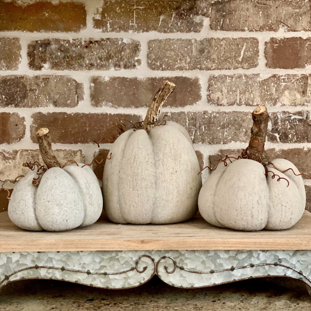 Concrete pumpkins on a riser in front of a brick wall.