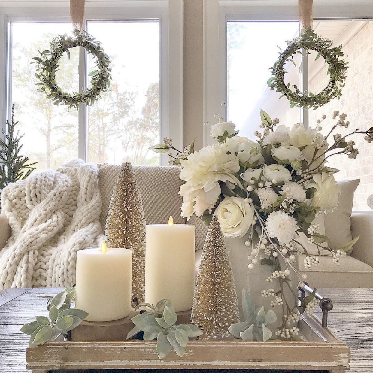 Tray on coffee table with candles, bottle brush Christmas trees and a white floral arrangement.