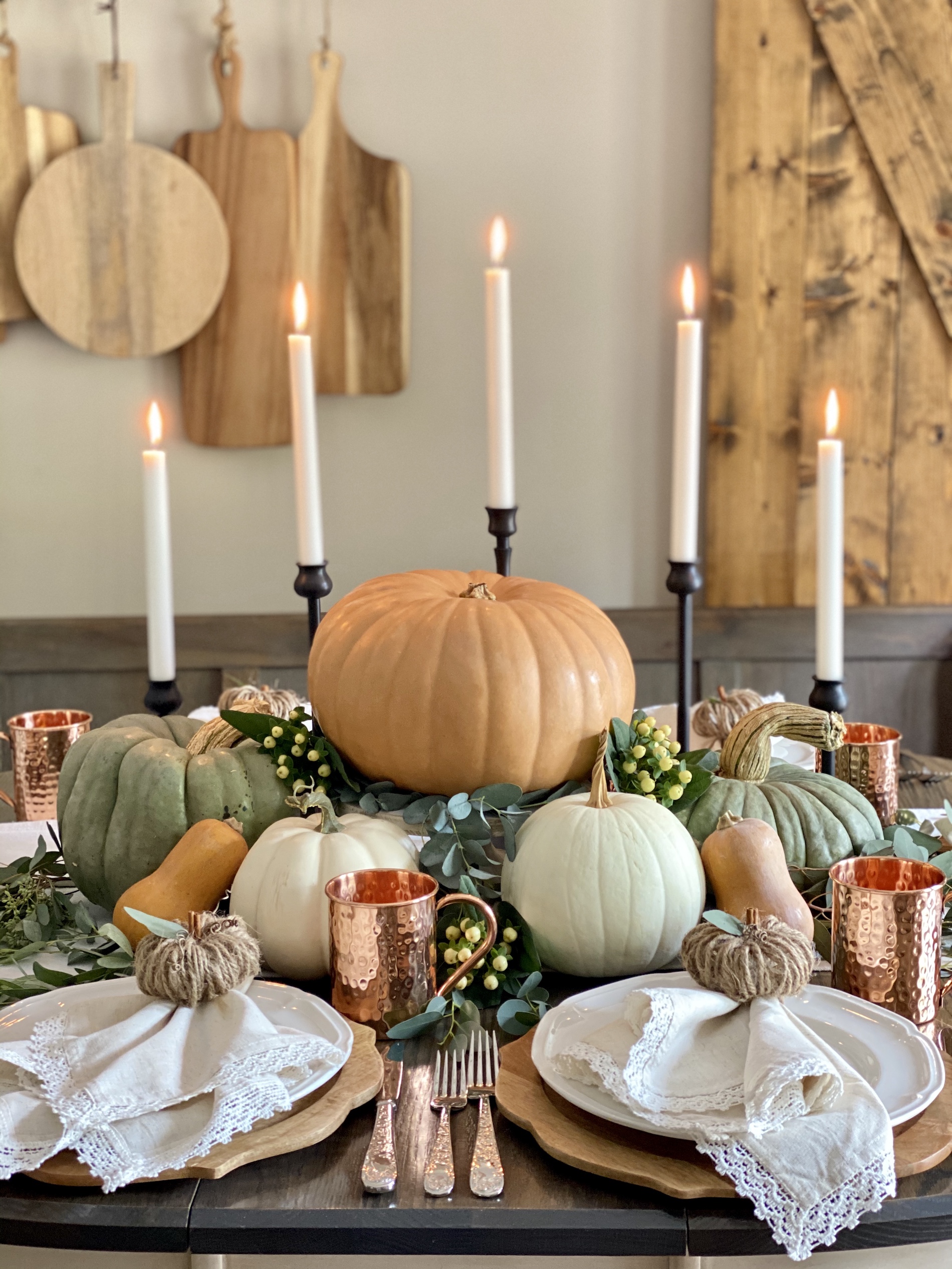 A Fall tablescape with a pumpkin centerpiece, candles and white dishes. 