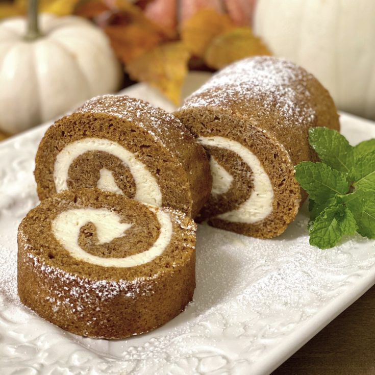 Pumpkin Roll on a white platter with a mint sprig garnish and pumpkins in a background.