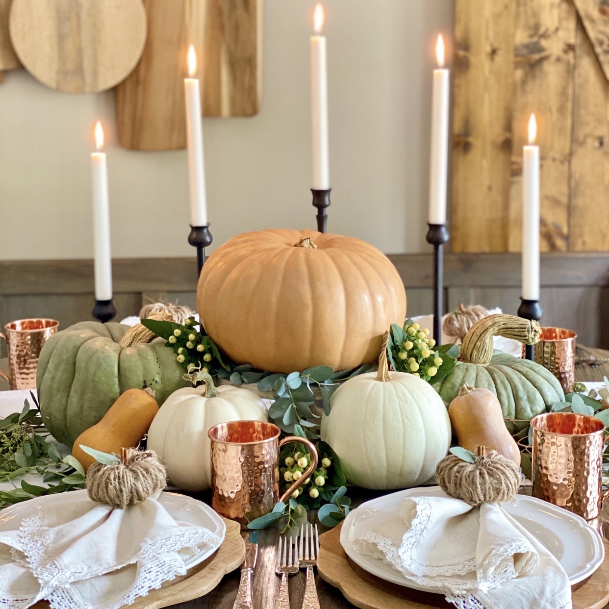 A table set for Fall with a pumpkin centerpiece, candles in black holders, and linen napkins on plates with twine pumpkin rings on them.