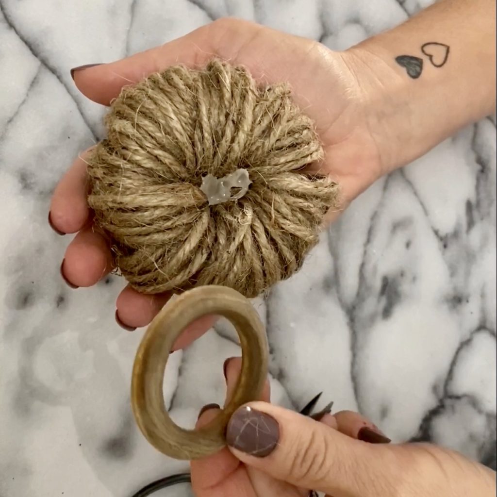 Using hot glue to attach the wood ring to the bottom of the twine pumpkin napkin ring.