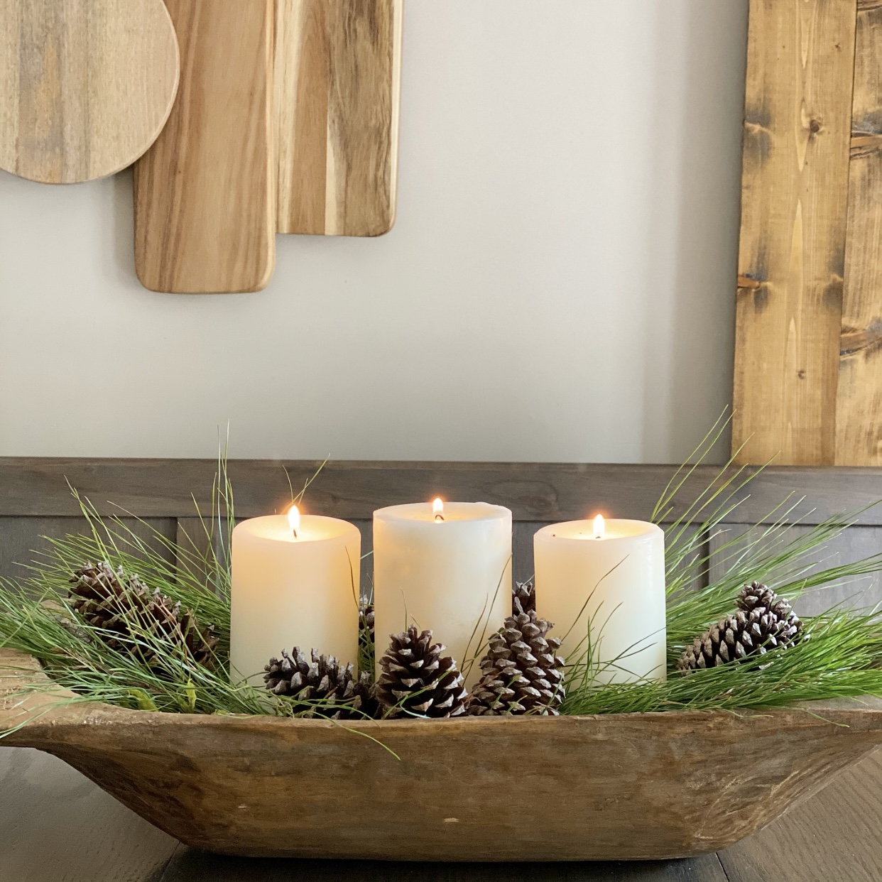 Dough bowl centerpiece with winter greens, pinecones, and candles.