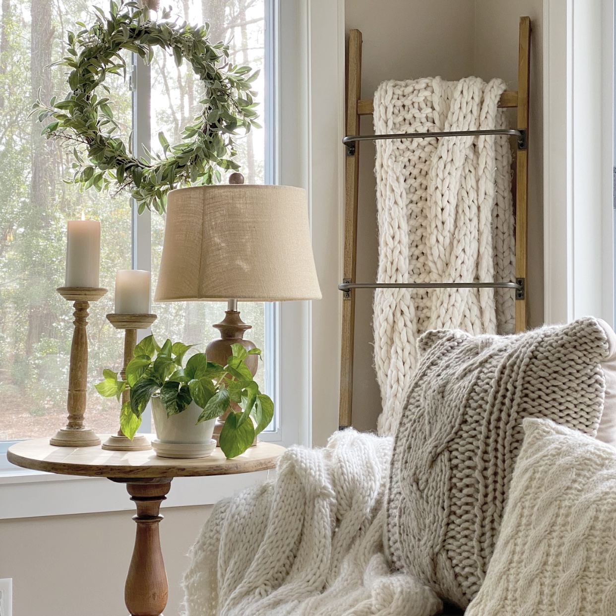 Cozy corner with knit blankets and candles on a side table with a green plant.
