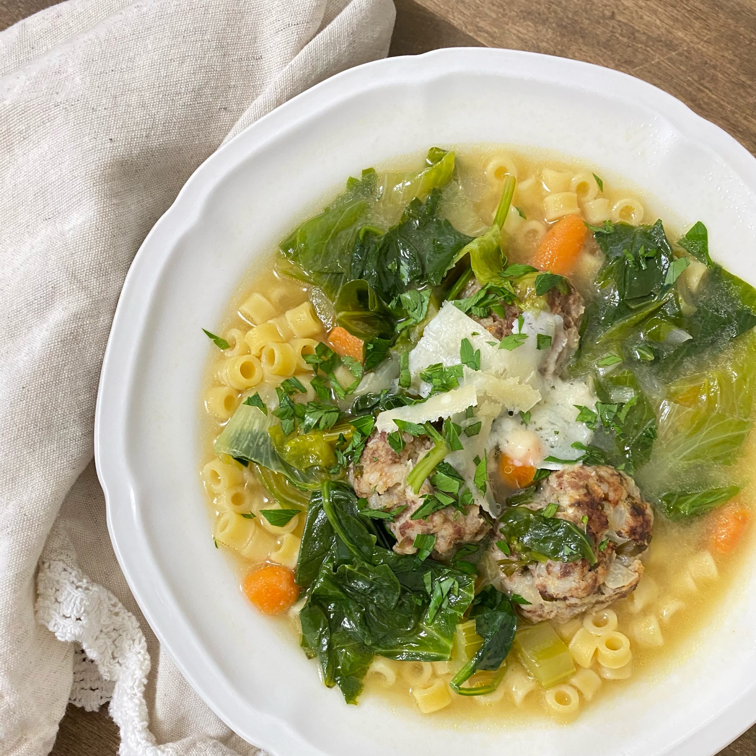 Italian Wedding Soup in a white bowl with a napkin on the side.