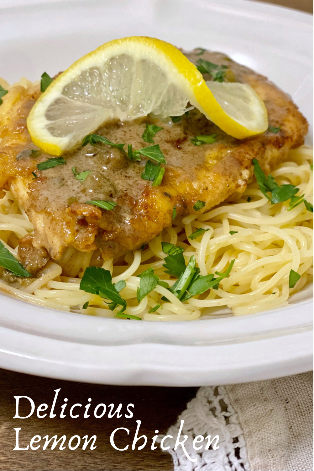 Lemon Chicken with capers on a bed of angel hair pasta garnished with parsley and a lemon wedge.