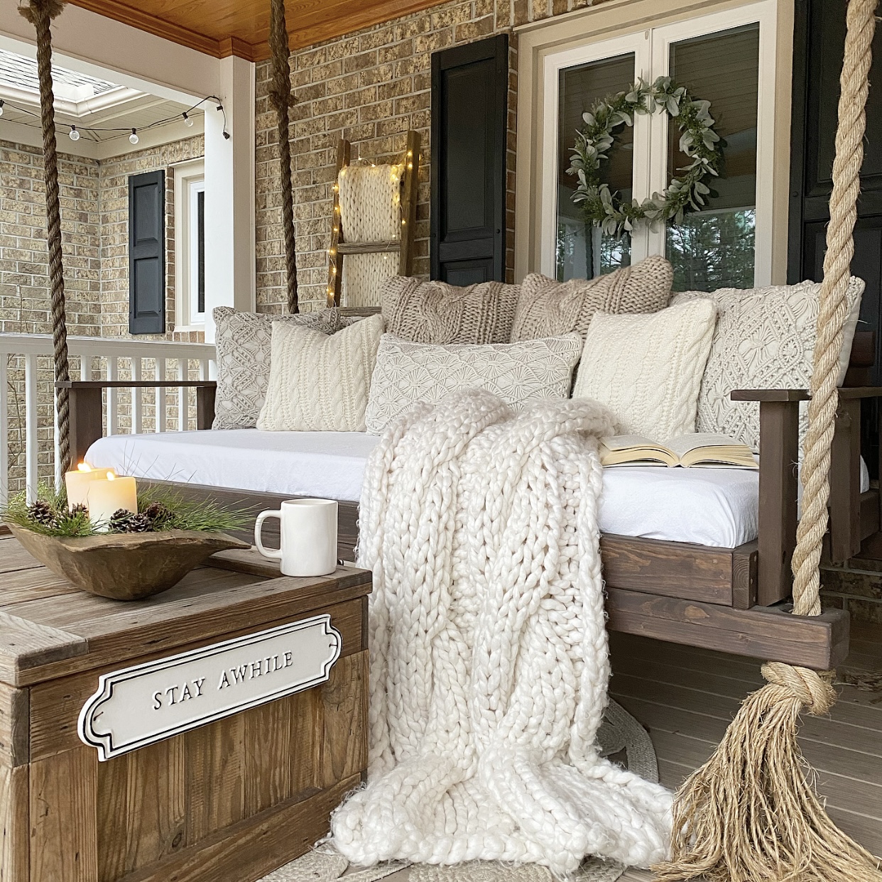 Wood front porch swing with cozy knit pillows and a blanket on it. 