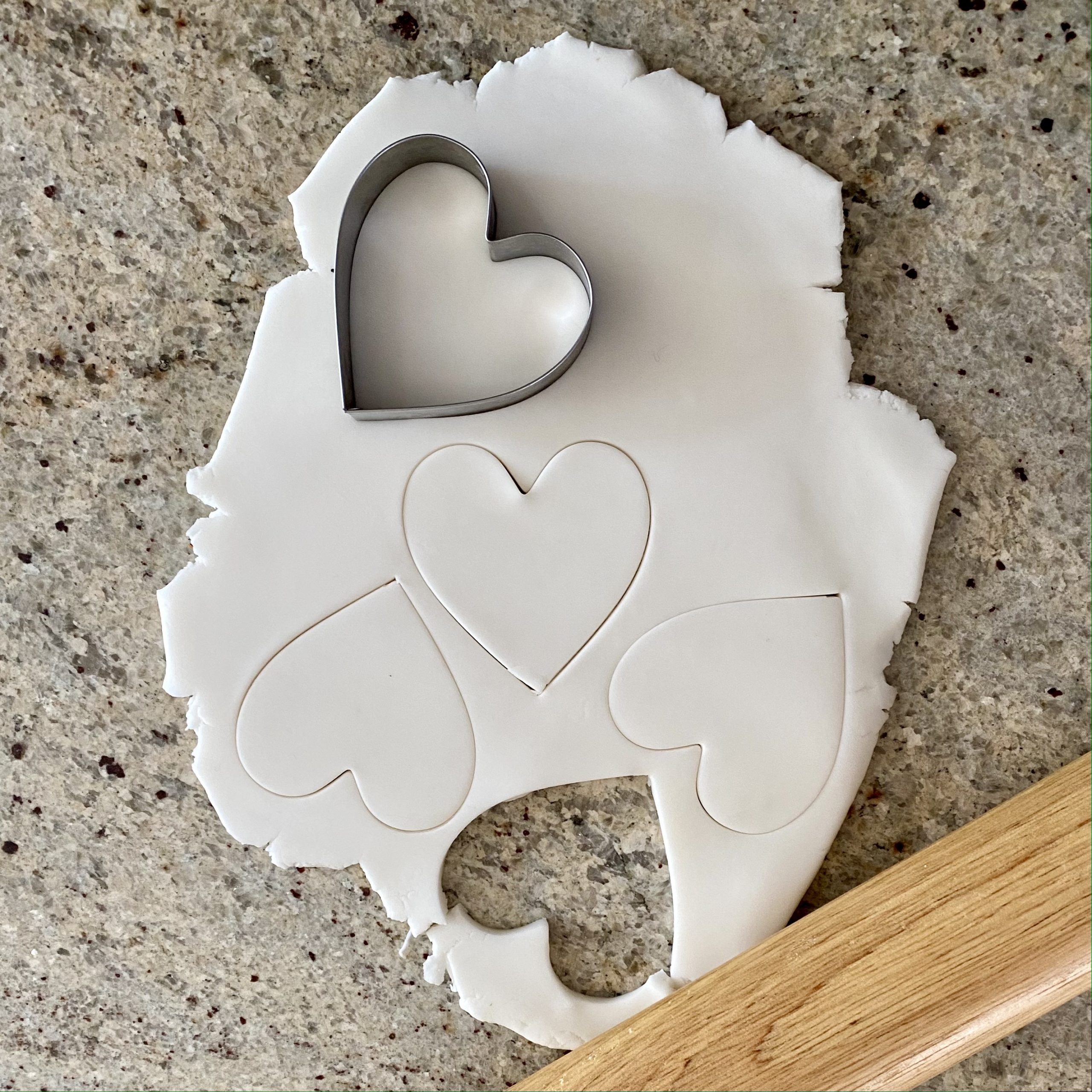 Baking soda dough rolled out and heart shapes are cut out of it with a cookie cutter.