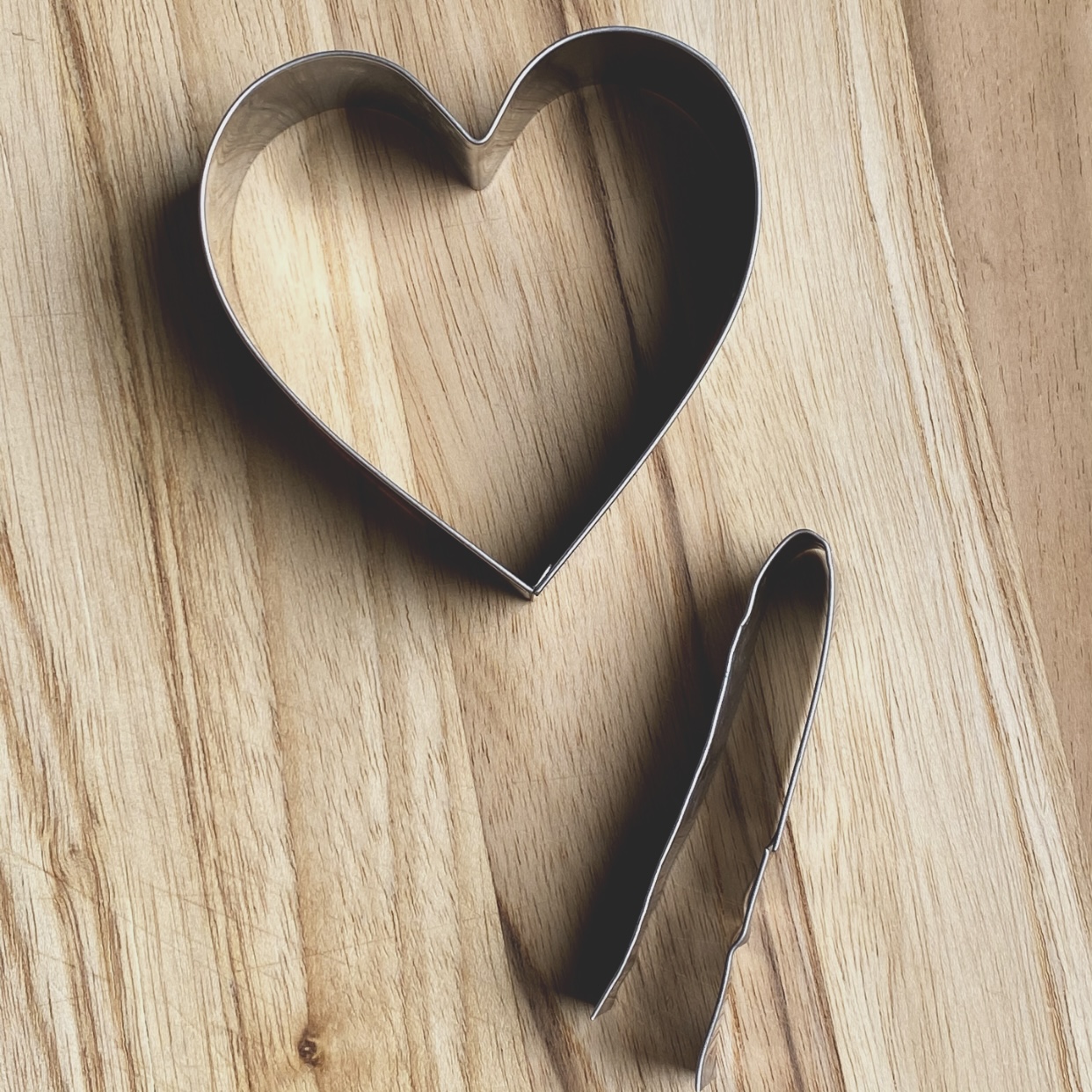 Heart shape cookie cutter with notch cutter on a wood board.
