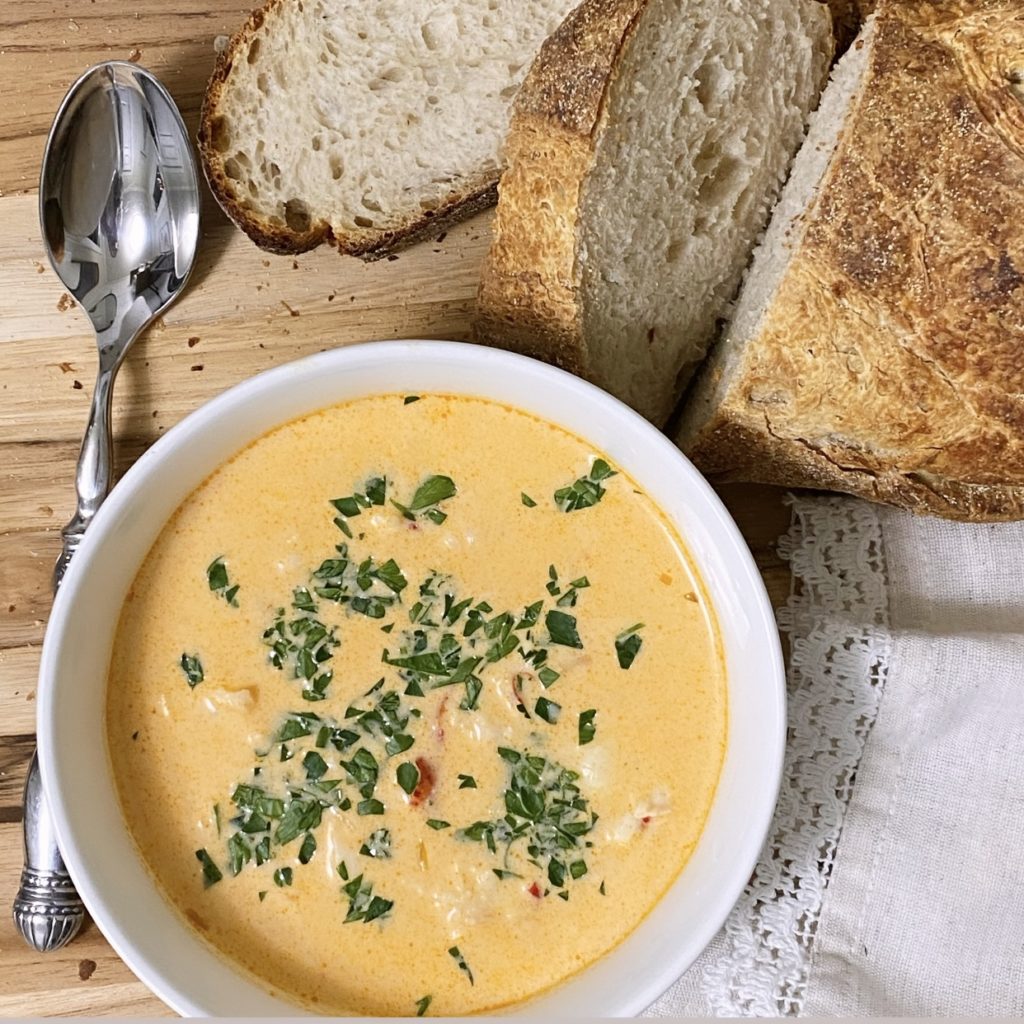 A white bowl of Lobster Bisque with sourdough bread and a spoon off to the side.