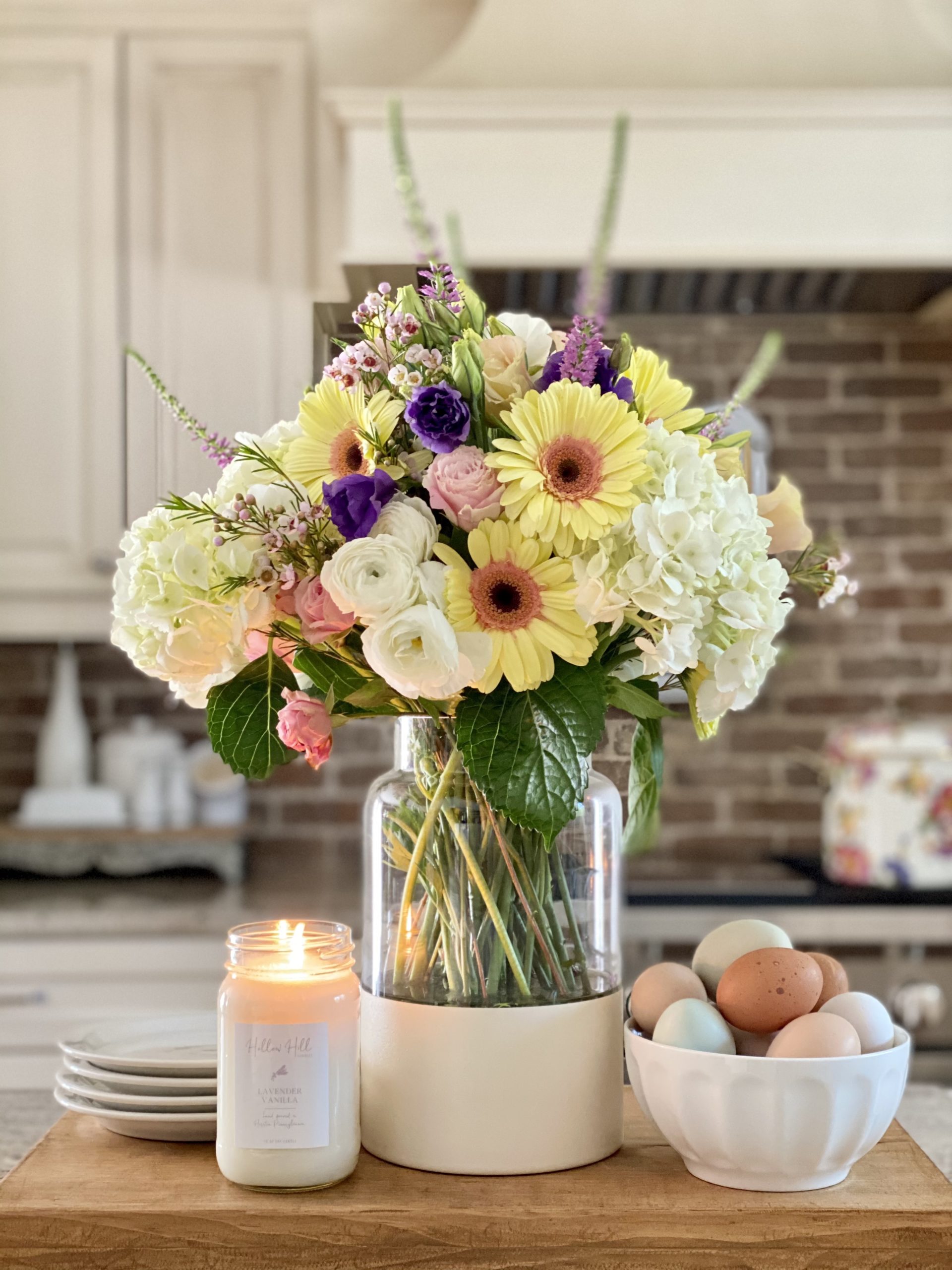 DIY color block vase in the kitchen on a wood riser with a beautiful spring bouquet, a candle, and a bowl of fresh eggs styled with it on the kitchen island.