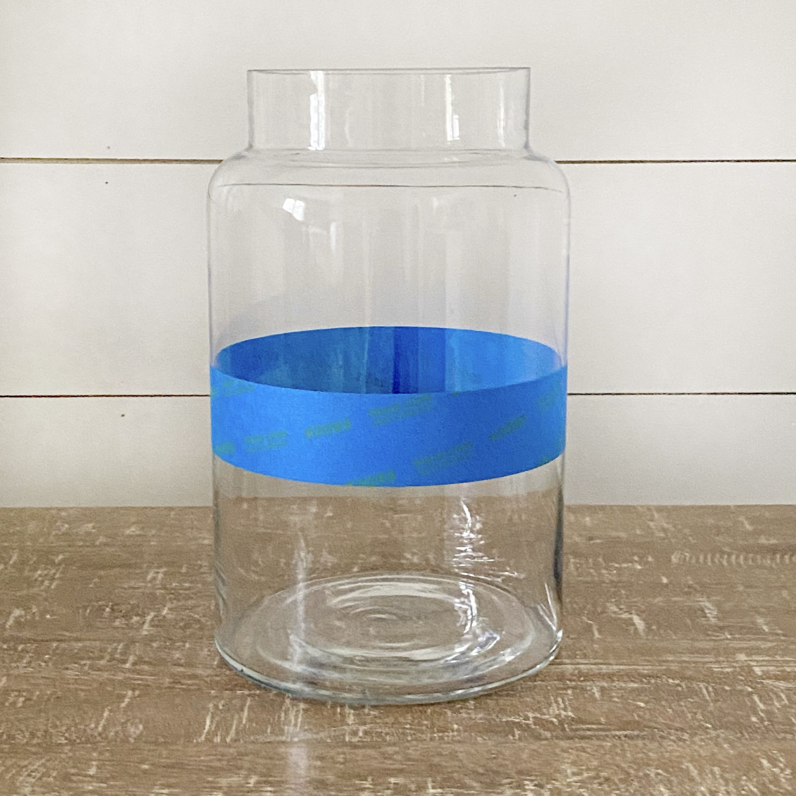 A glass vase with painters tape marking where the paint will be applied to the vase.