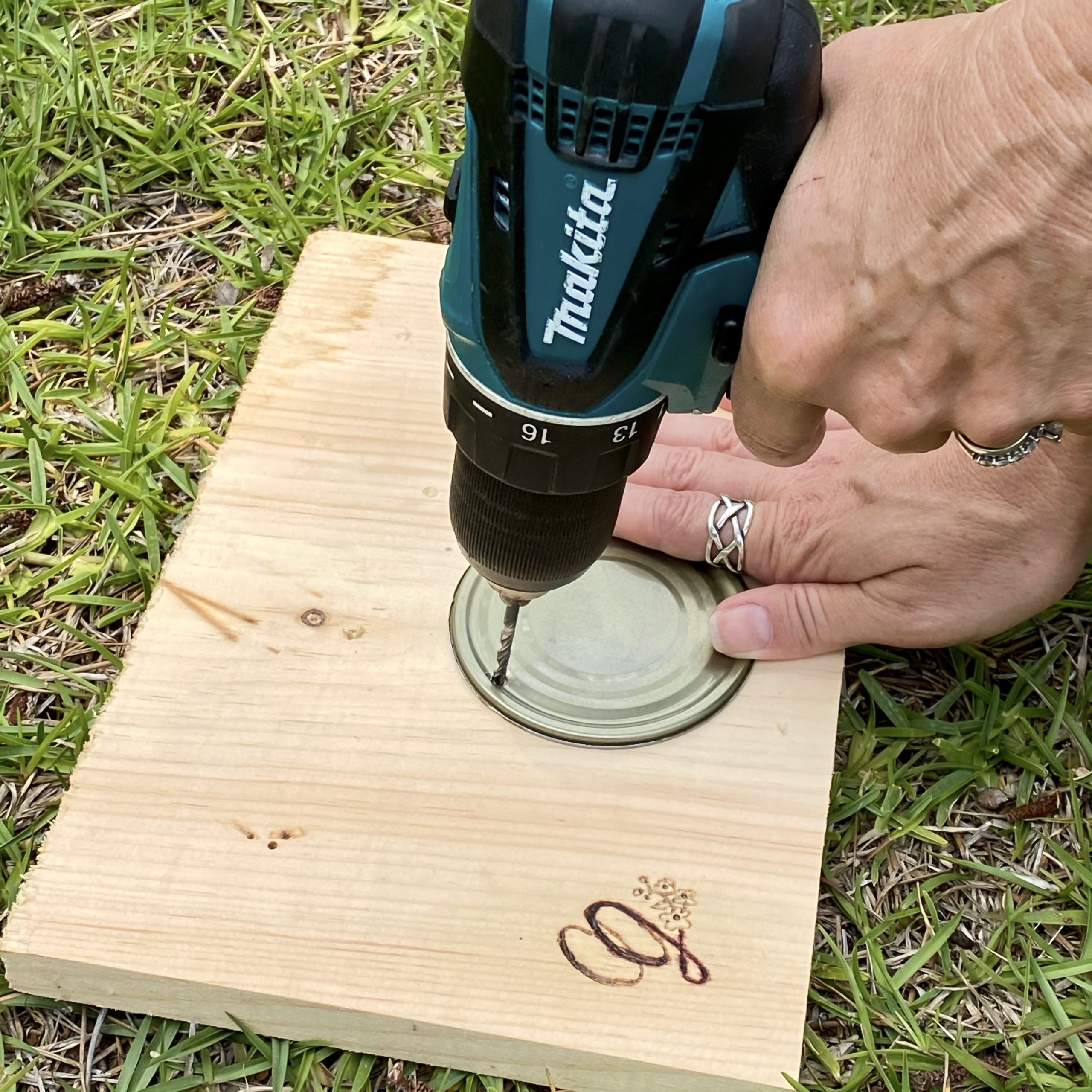 Drilling a hole in the tin can top to make a DIY garden marker.