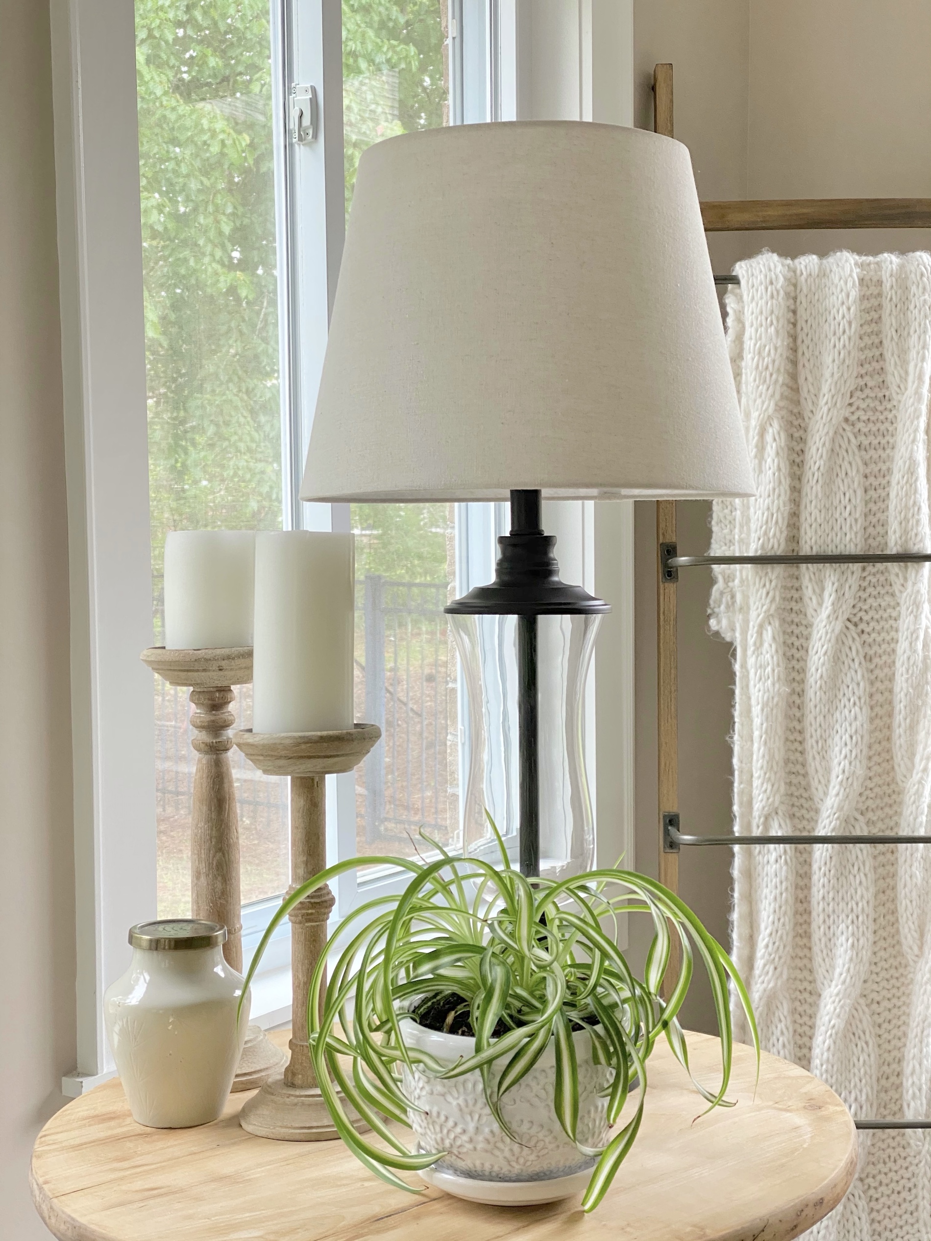Spider plant on a side table in a white planter styled with a lamp and candlesticks.