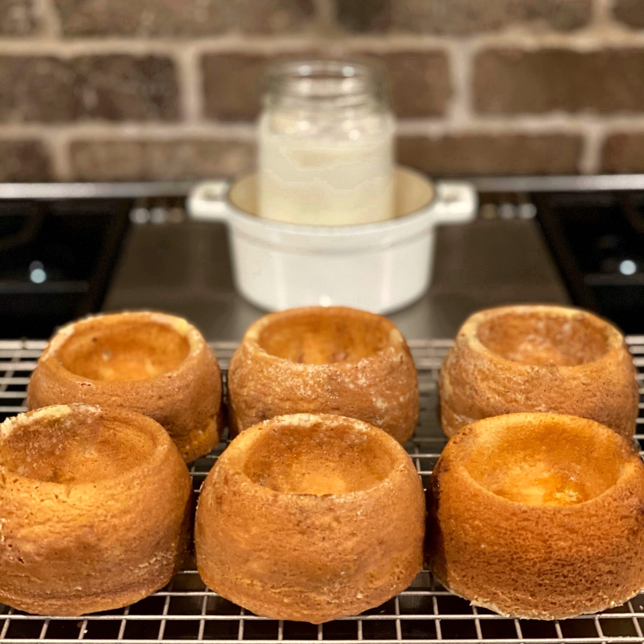 Six vanilla cake bowls cooling on a wire rack on the stove top.