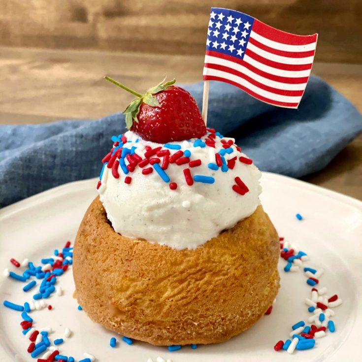 A vanilla cake bowl with vanilla ice cream inside decorated with red, white, and blue sprinkles and a strawberry on top.