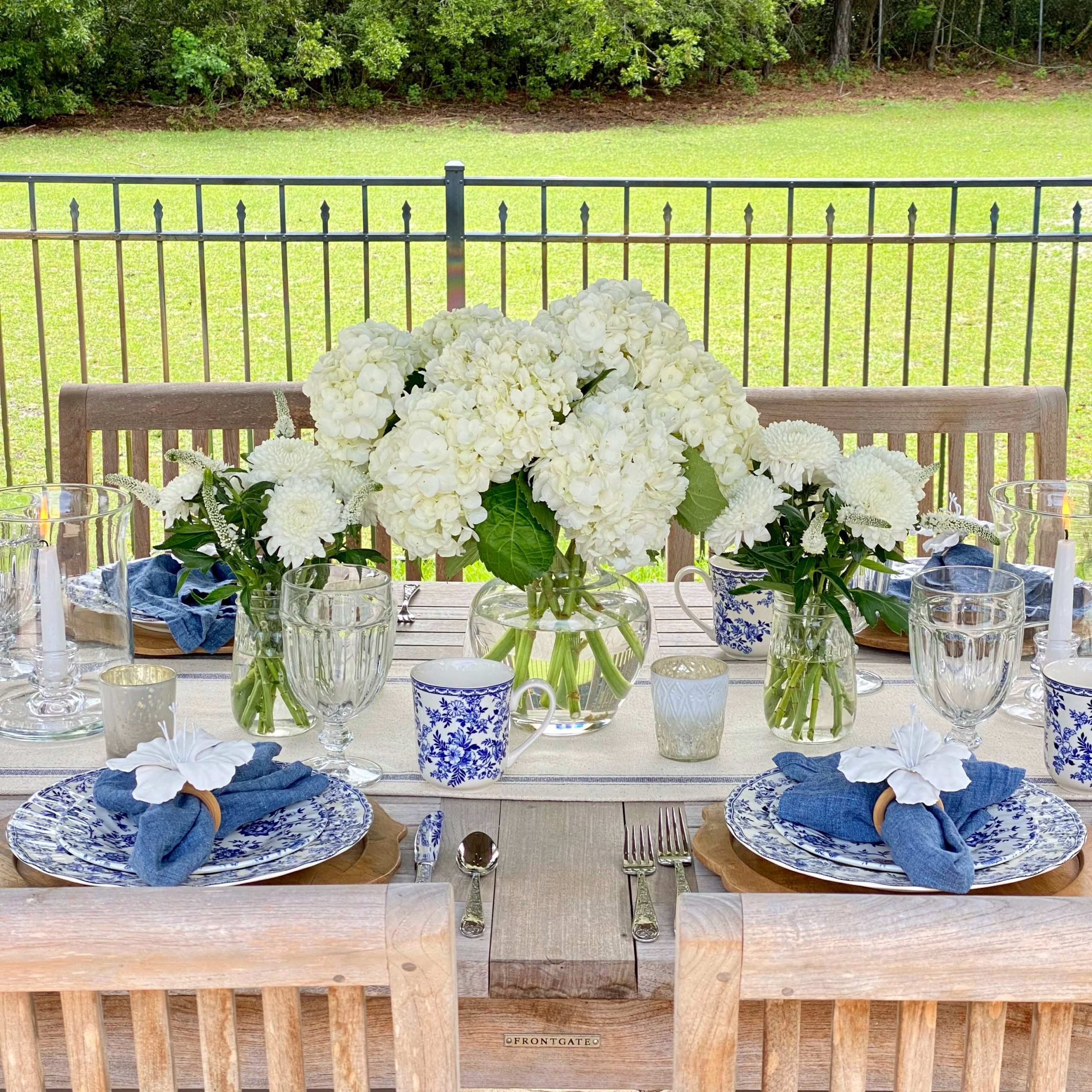 Blue and white outdoor tablescape with focus on the white floral centerpieces.
