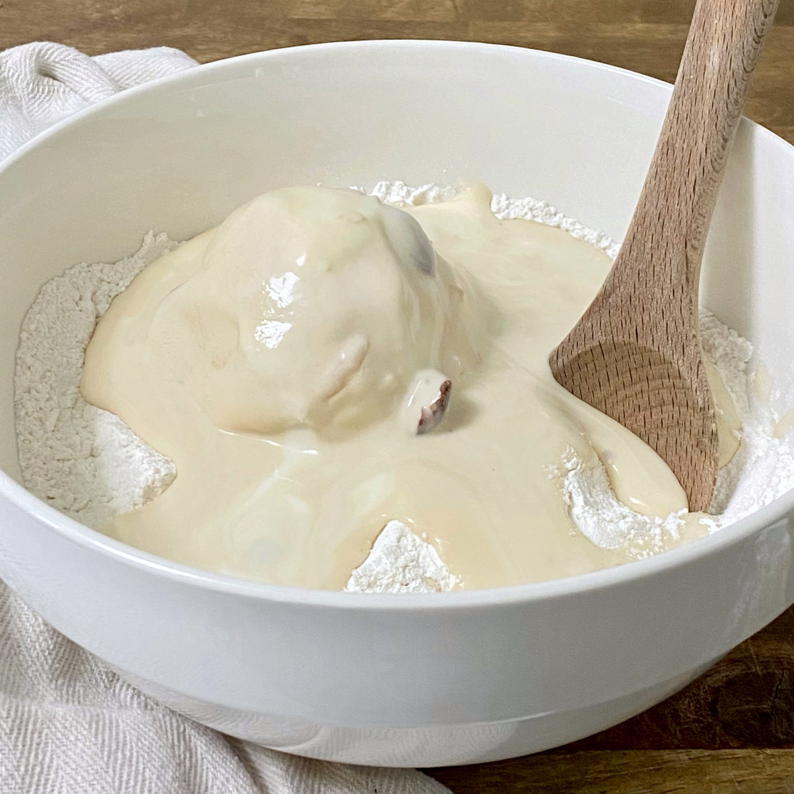 Flour and ice cream in a white mixing bowl with a wooden spoon.