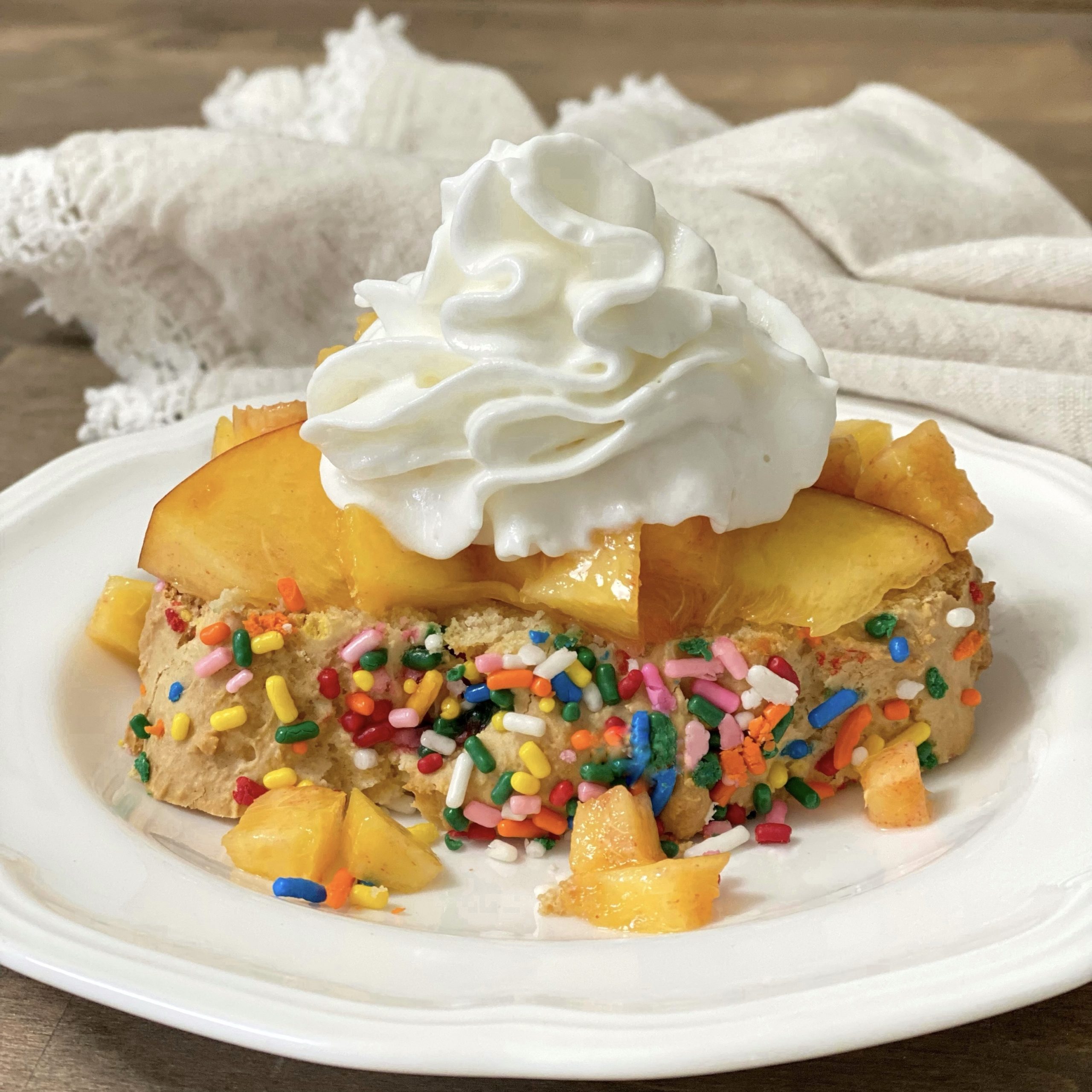 Ice cream bread with sprinkles on a white plate with peaches and whipped cream.