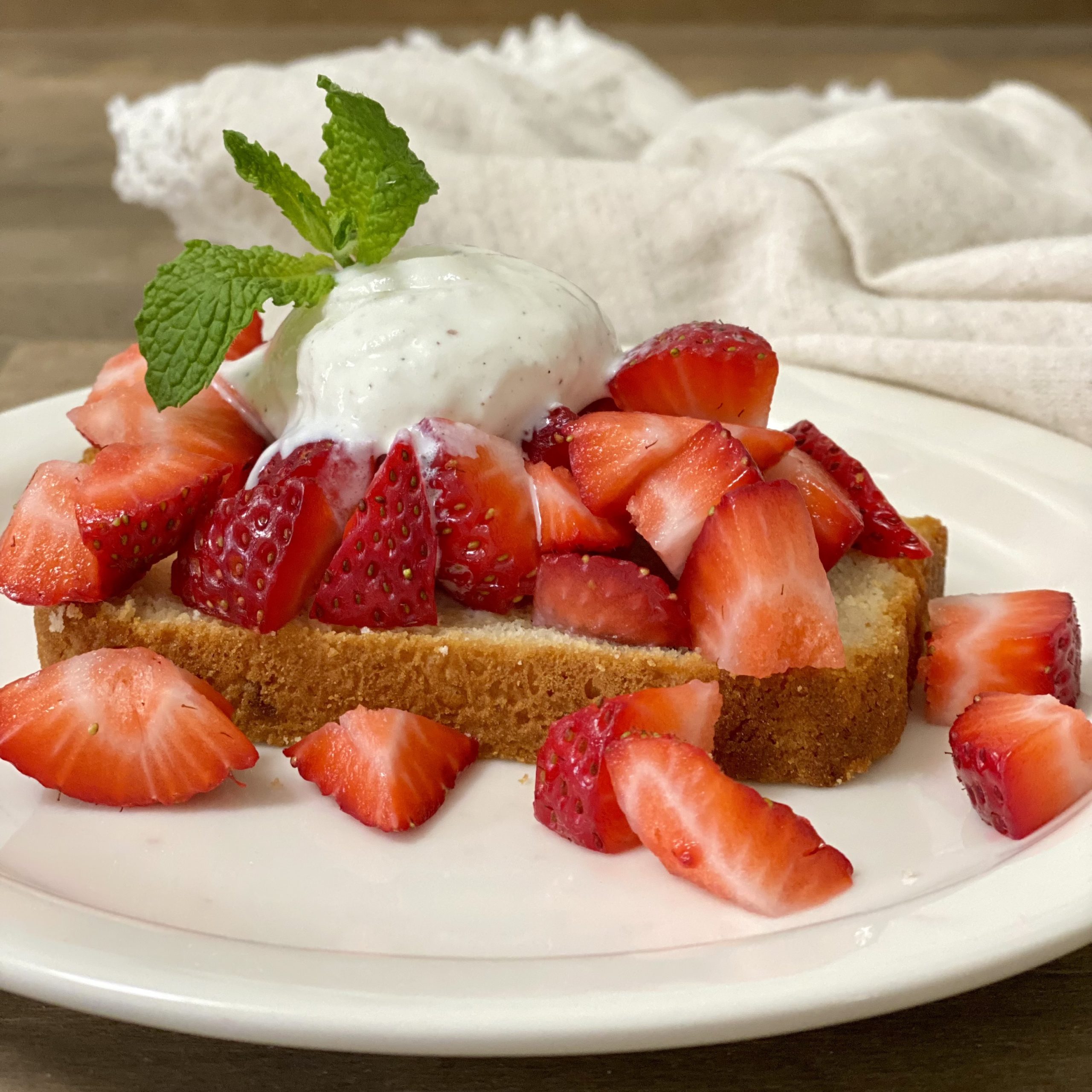 A slice of ice cream bread with strawberries and vanilla ice cream on top. Garnished with a mint spring on a white plate.