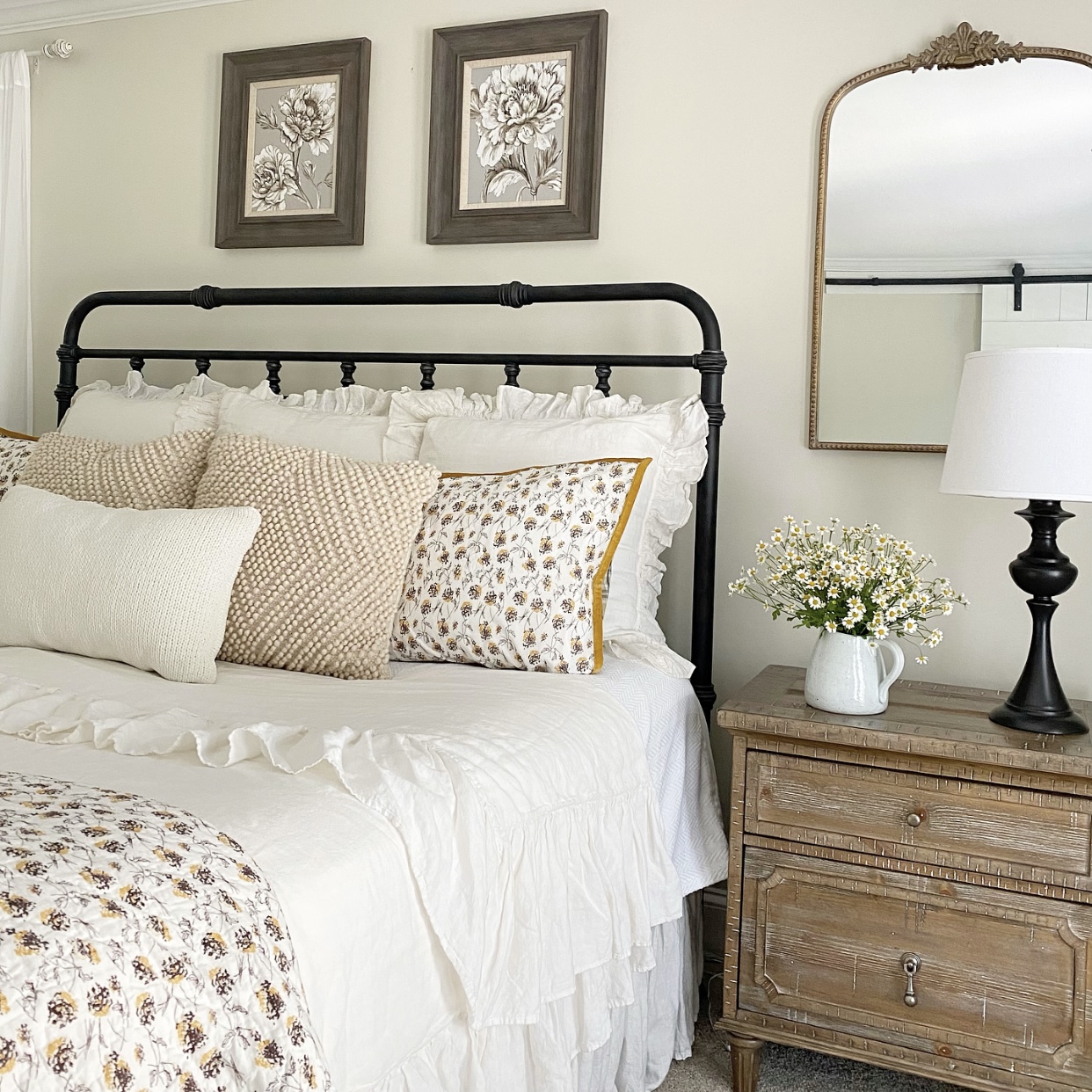 Farmhouse bedroom with black iron bed frame, white, yellow, and brown floral bedding and lots of pillows.