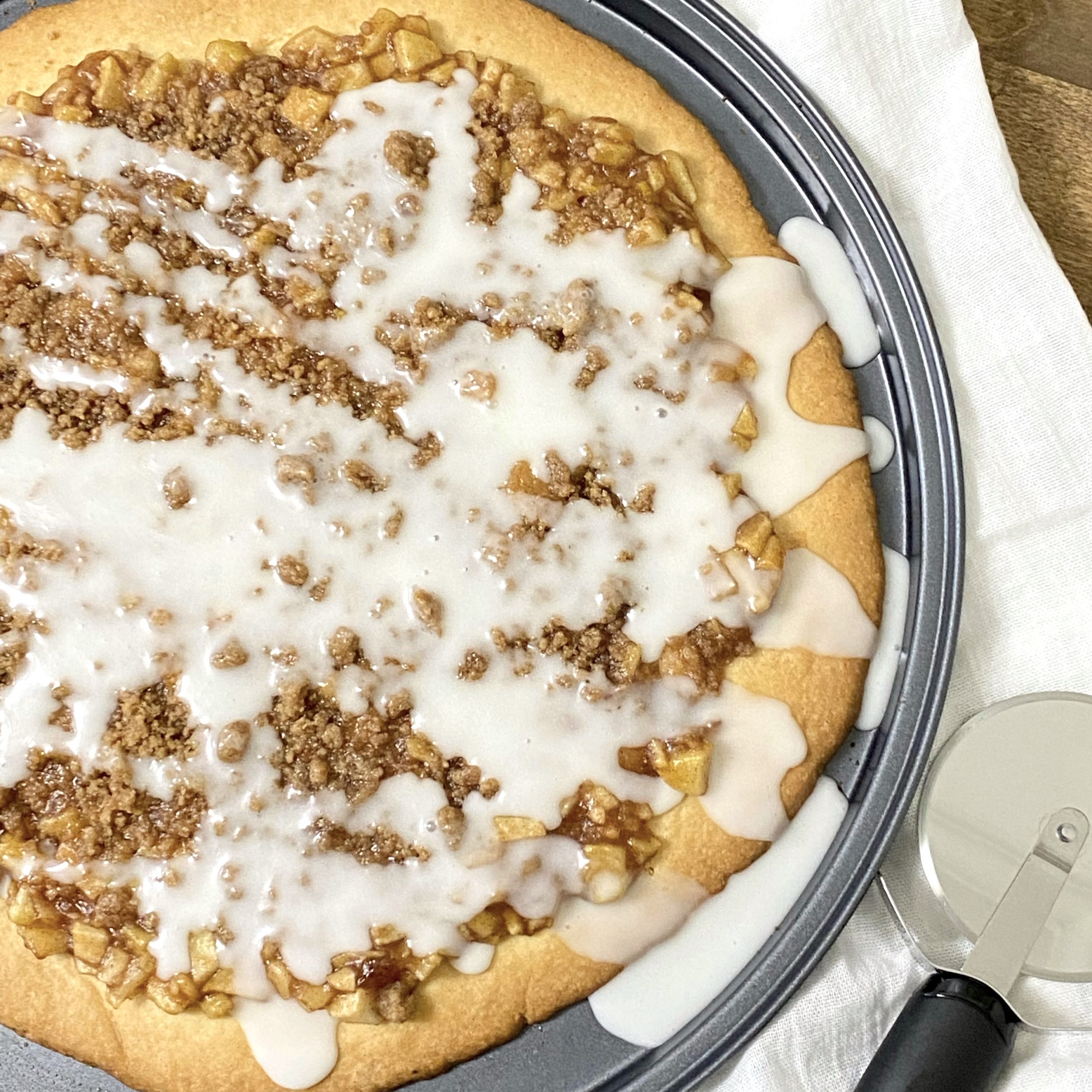 Apple pie pizza with a pizza cutter next to it on the counter.