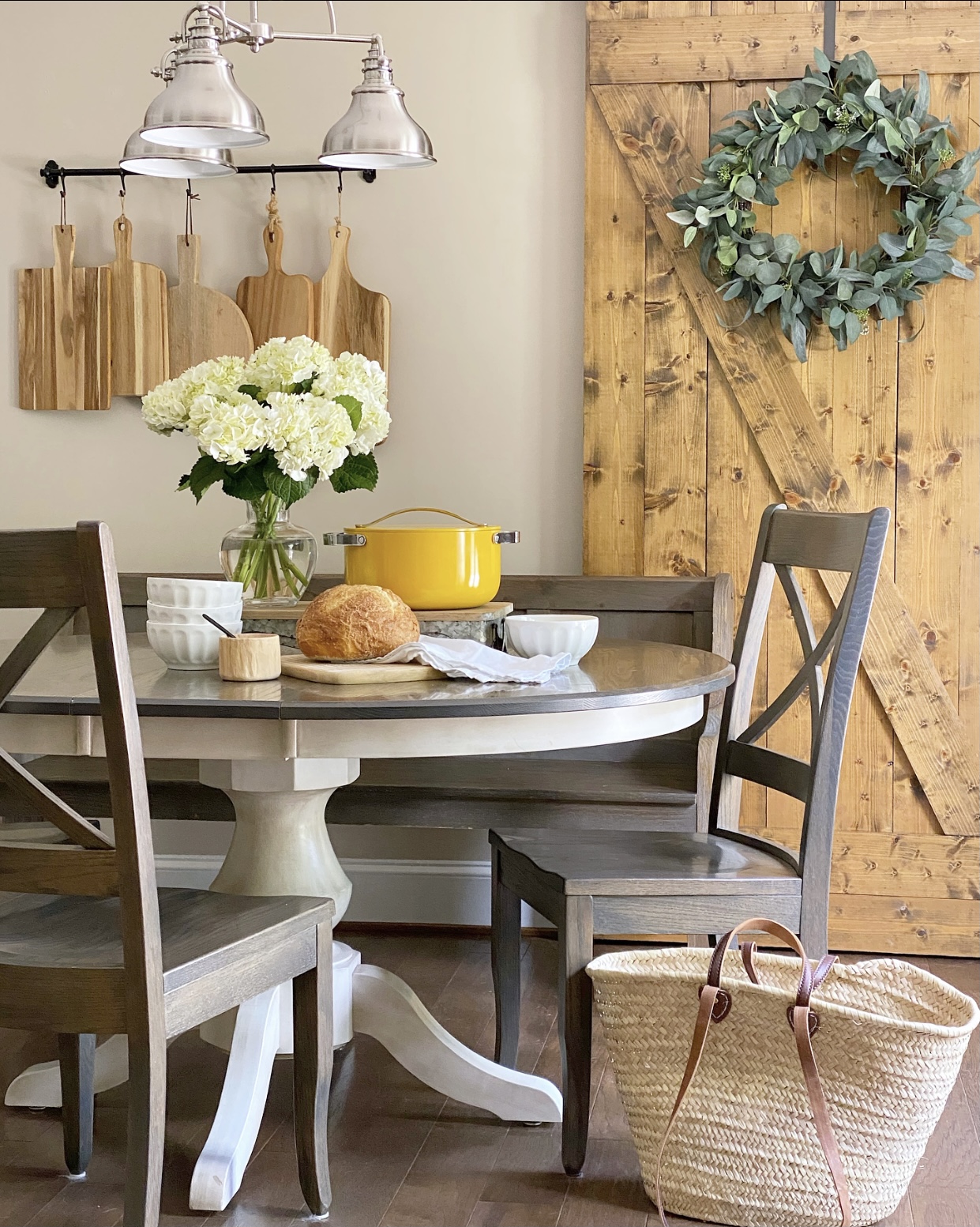 Breakfast nook with a centerpiece on the table including white flowers in a vase, a yellow Dutch oven, and fresh baked bread with soup bowls.