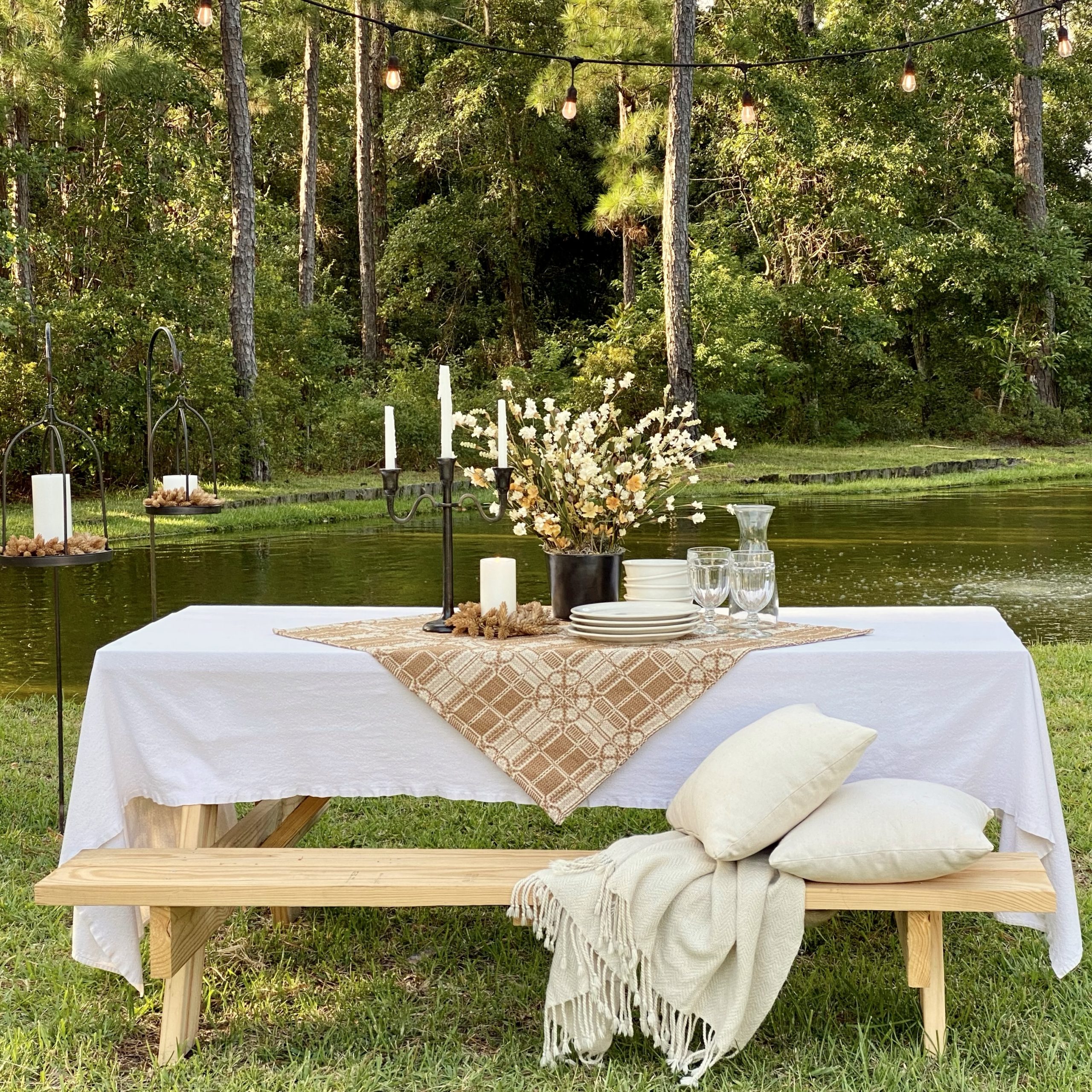 Picnic table by the pond decorated for early Fall with table cloths, candles, fall florals, plates, bowls and glasses.