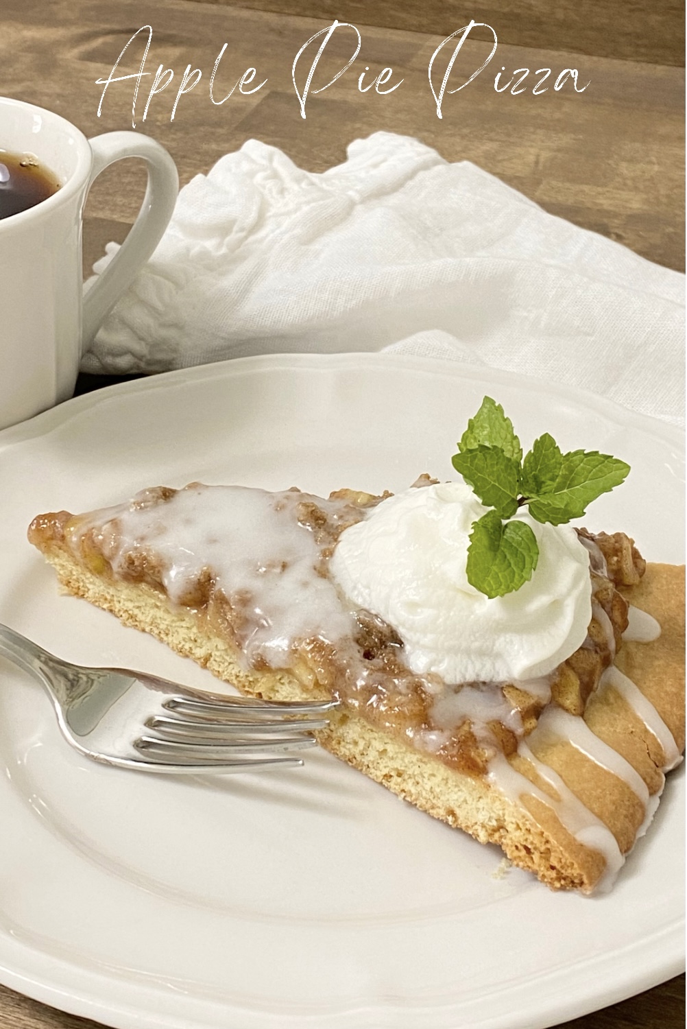 A Pinterest Pin for Apple Pie Pizza. A slice of apple pie pizza with a dollop of whipped cream and a mint sprig on a white a white plate.