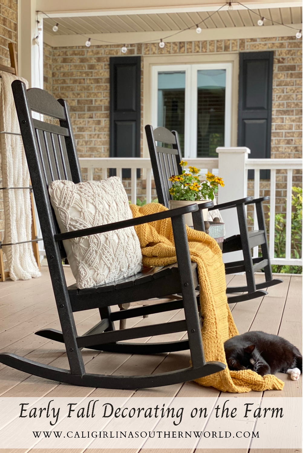 Pinterest Pin of two black rocking chairs on the front porch. One has a cream macrame pillow and a muted gold knit blanket on it. In front of the rocker is a black cat napping.