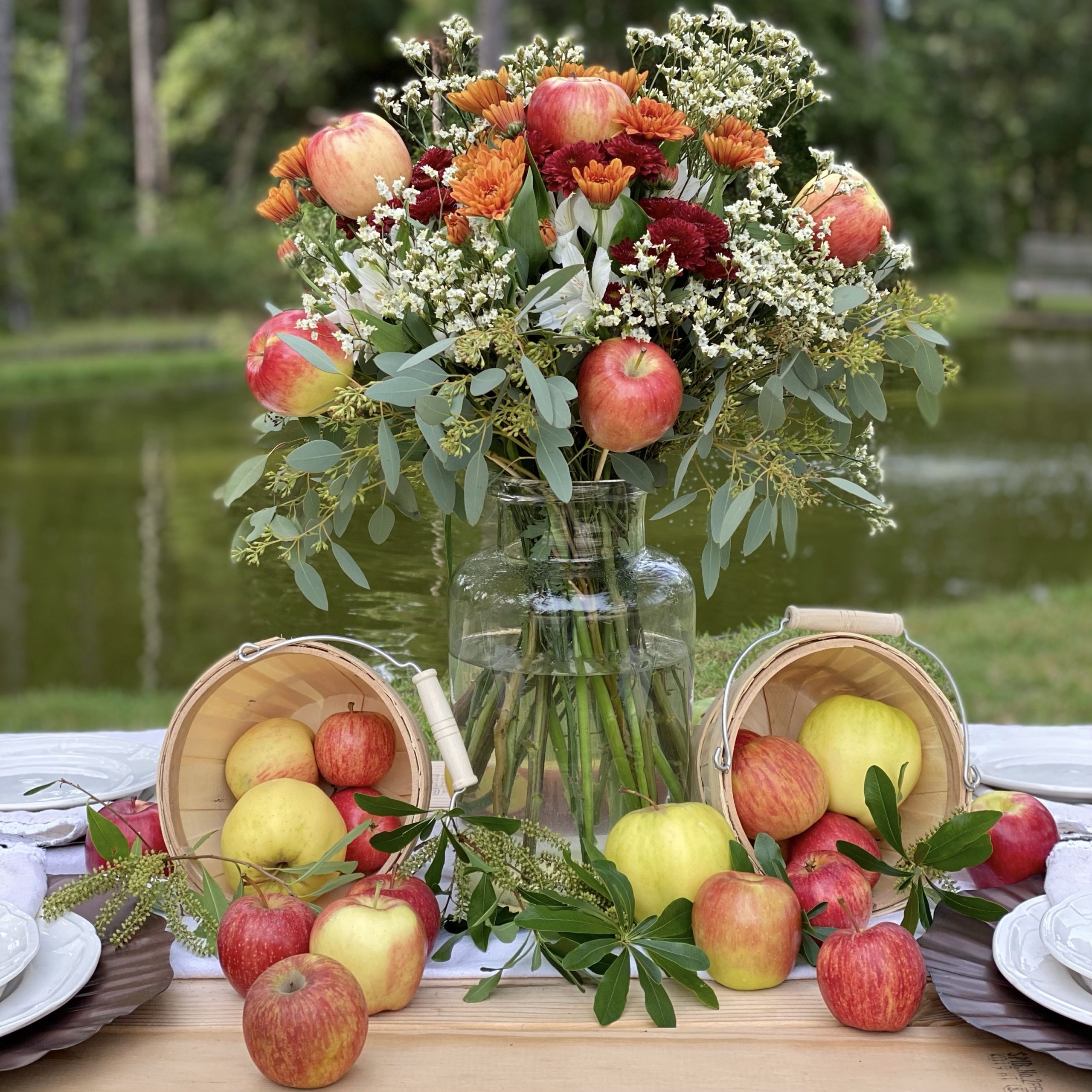 Apple floral arrangement surrounded by bushel baskets filled with apples.