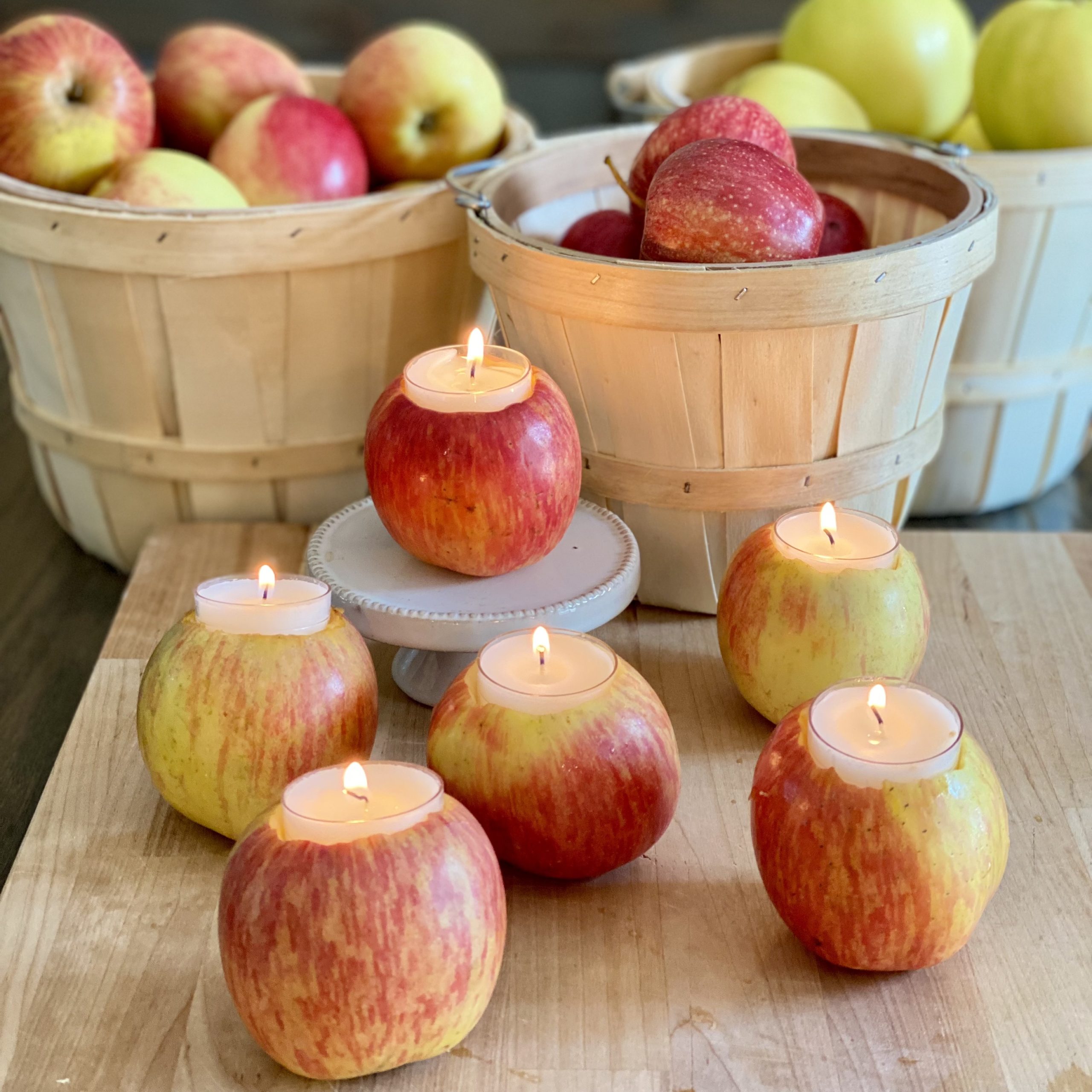 Apples cored out with votive candles on top. In the background are orchard baskets filled with apples.