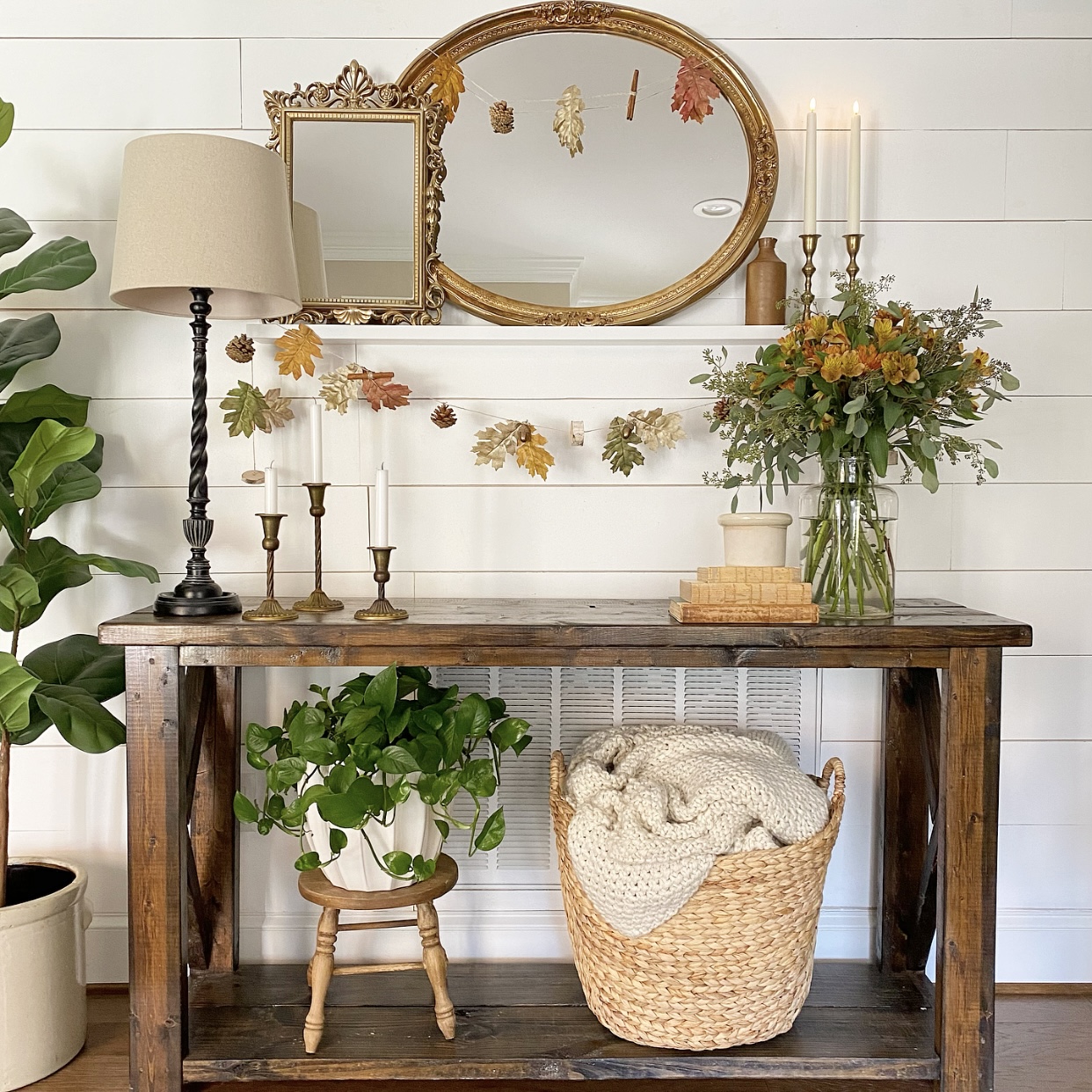Table in foyer with shelf on the wall above it. Shelf holds layered vintage mirrors and easy Fall garland hanging from them.