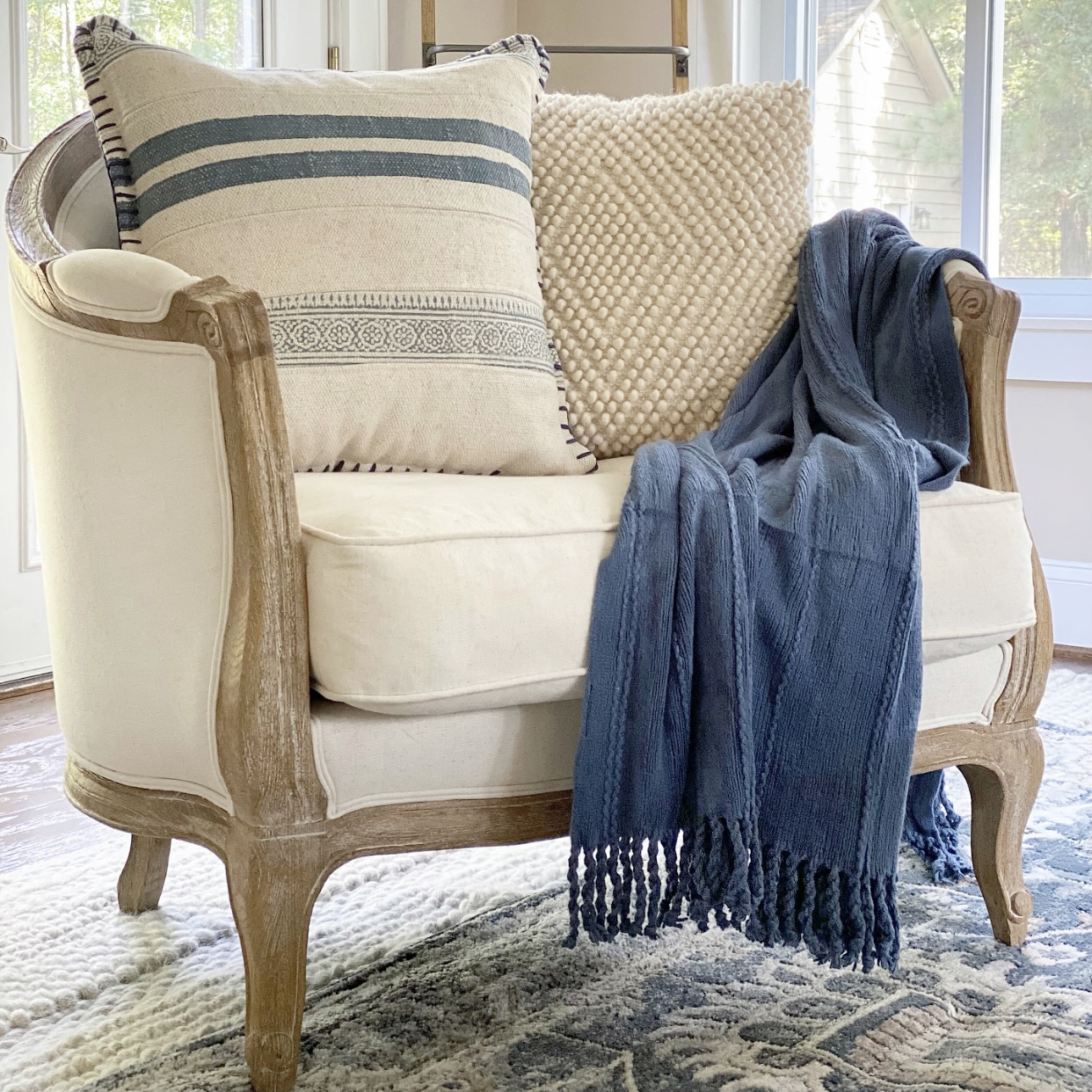 Blue knit blanket draped over the arm of a white and wood club chair.
