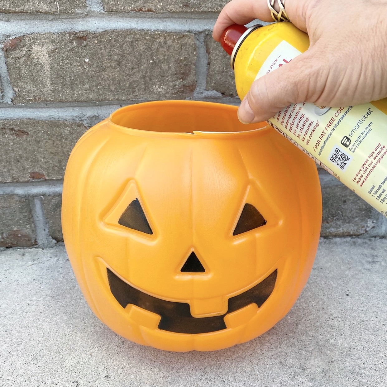 Spraying cooking spray inside an orange plastic trick or treat plastic pail.