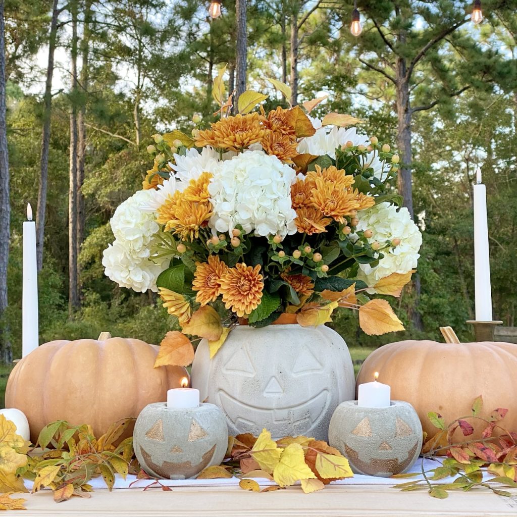 DIY concrete jack o'lanterns used in a centerpiece on the table as candle holders and a vessel for a fall floral arrangement.