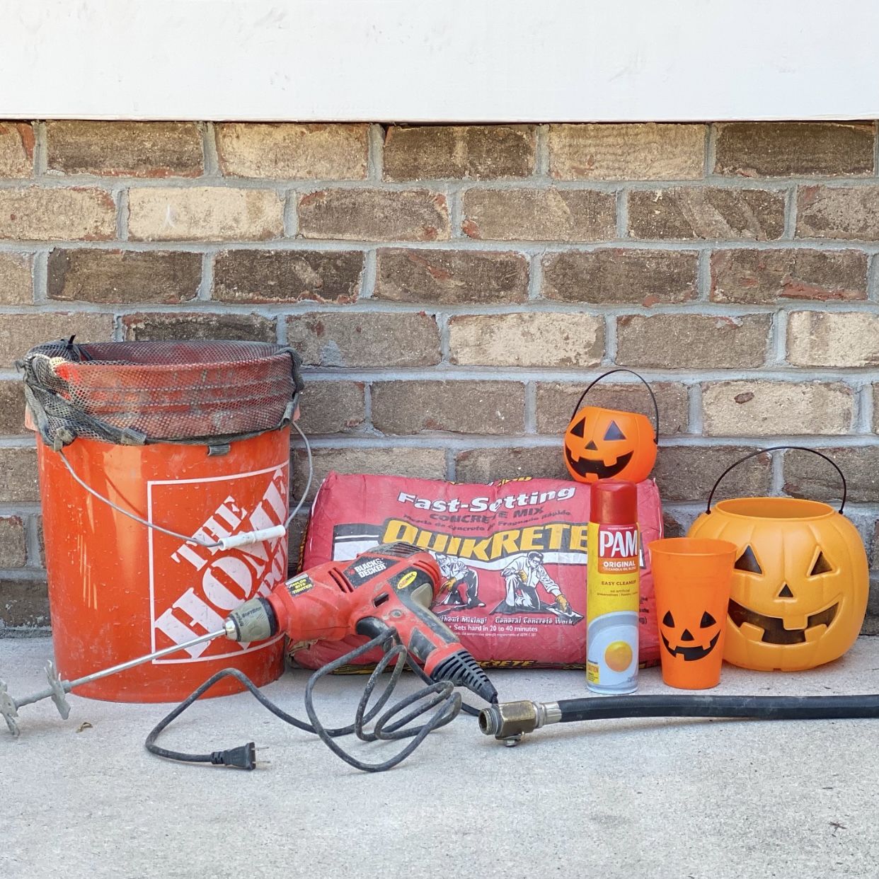 Everything you need to make DIY Concrete Jack O'Lanterns including concrete, jack o'lantern trick or treat pail, a plastic cup, and a bucket.