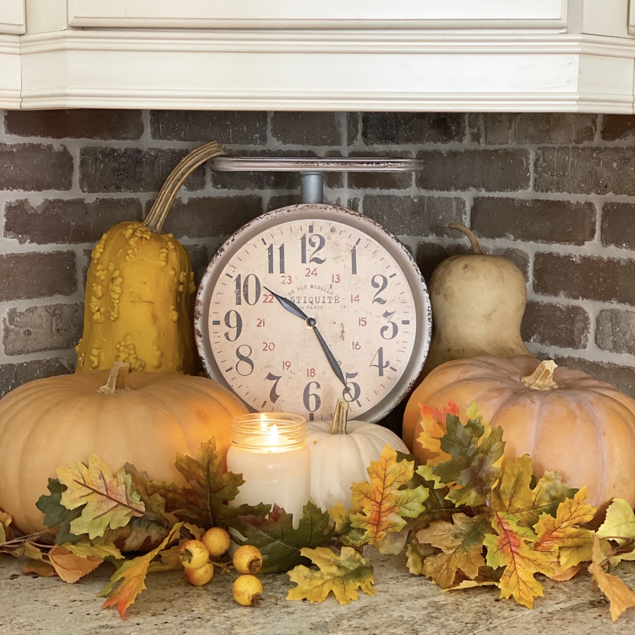 Clock, pumpkins, candle and leaves making a vignette on the kitchen counter in a corner.