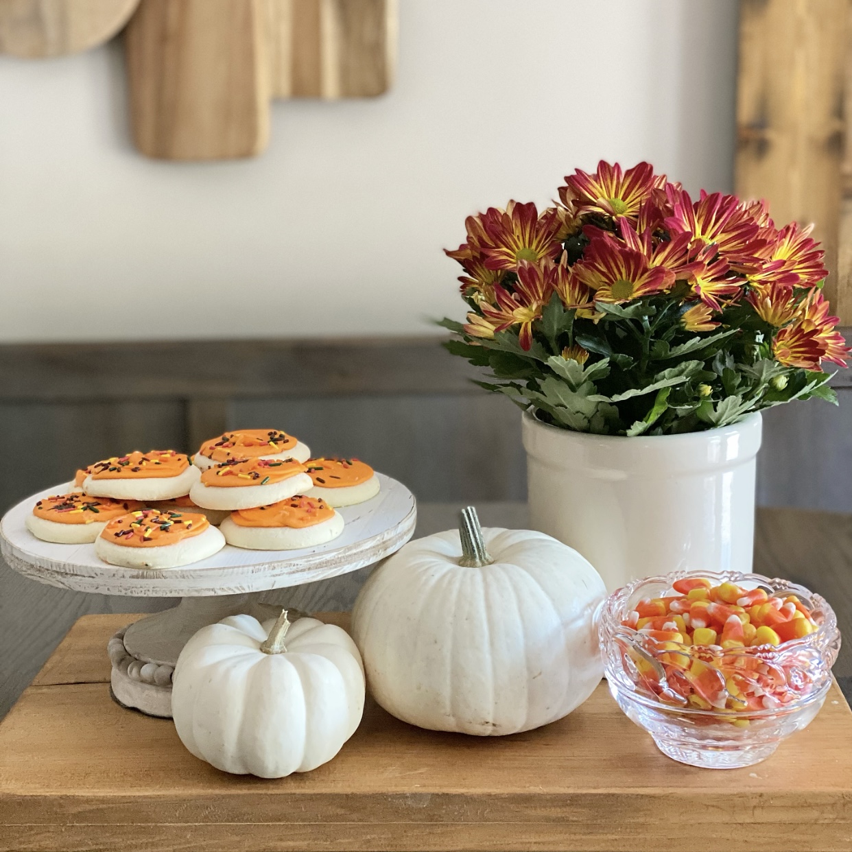 Fall vignette on the kitchen table with mums, pumpkins, cookies, and candy corn.