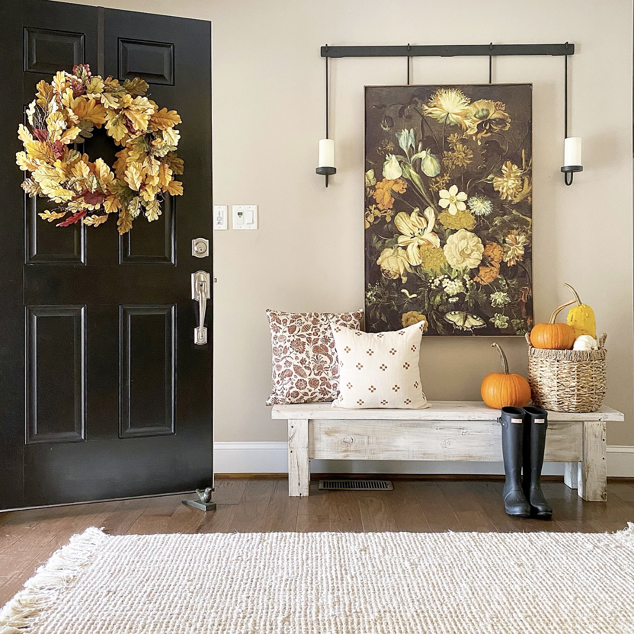 Farmhouse foyer with open front door. On the front door is a fall wreath. A bench in front of the door with pillows and pumpkins on it.